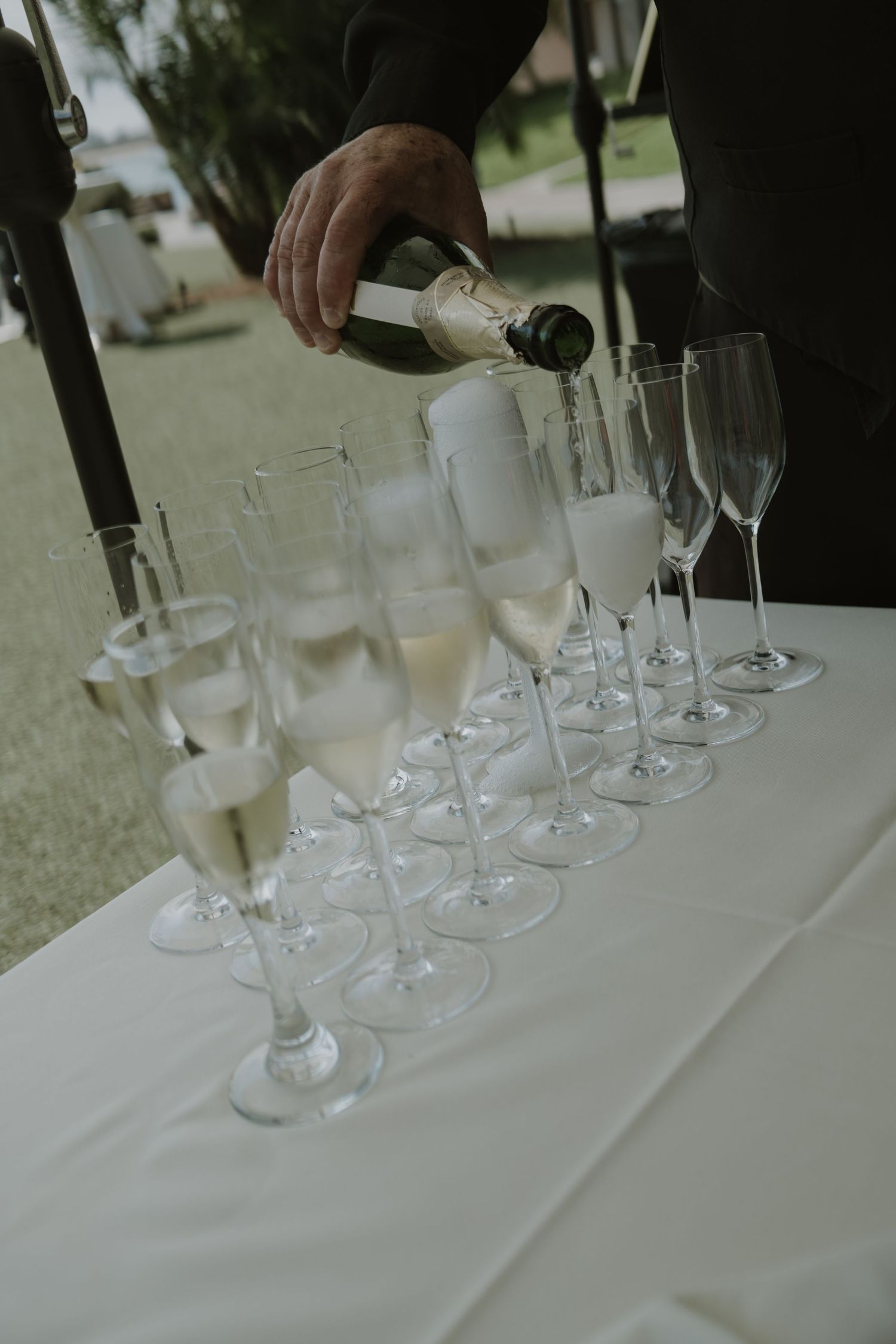 Hands pouring drinks into champagne glasses on white tablecloth.