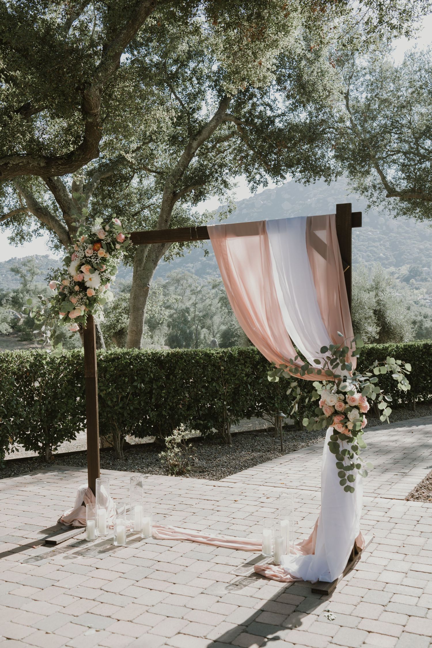 Rustic wooden wedding arch adorned with blush pink draping and floral arrangements outdoors.