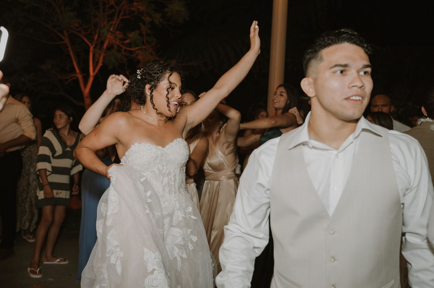 Bride in strapless lace gown dancing joyfully with groom at outdoor wedding reception.