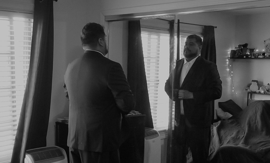 Two men in suits having a conversation in a dimly lit room with window blinds in black and white photo.