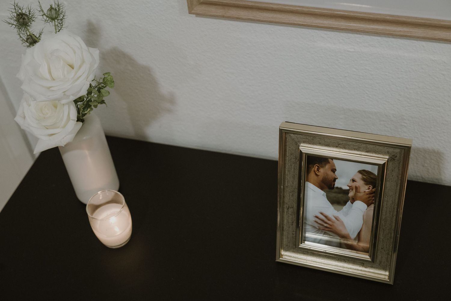A framed couple photo beside a white rose vase on a dark table, perfect for romantic home decor inspiration.