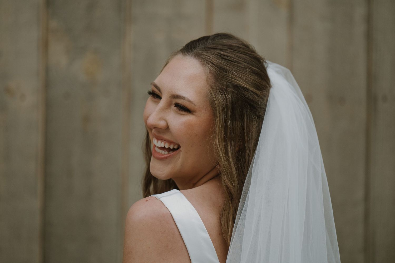 Smiling bride in white dress and veil laughing joyfully on her wedding day.