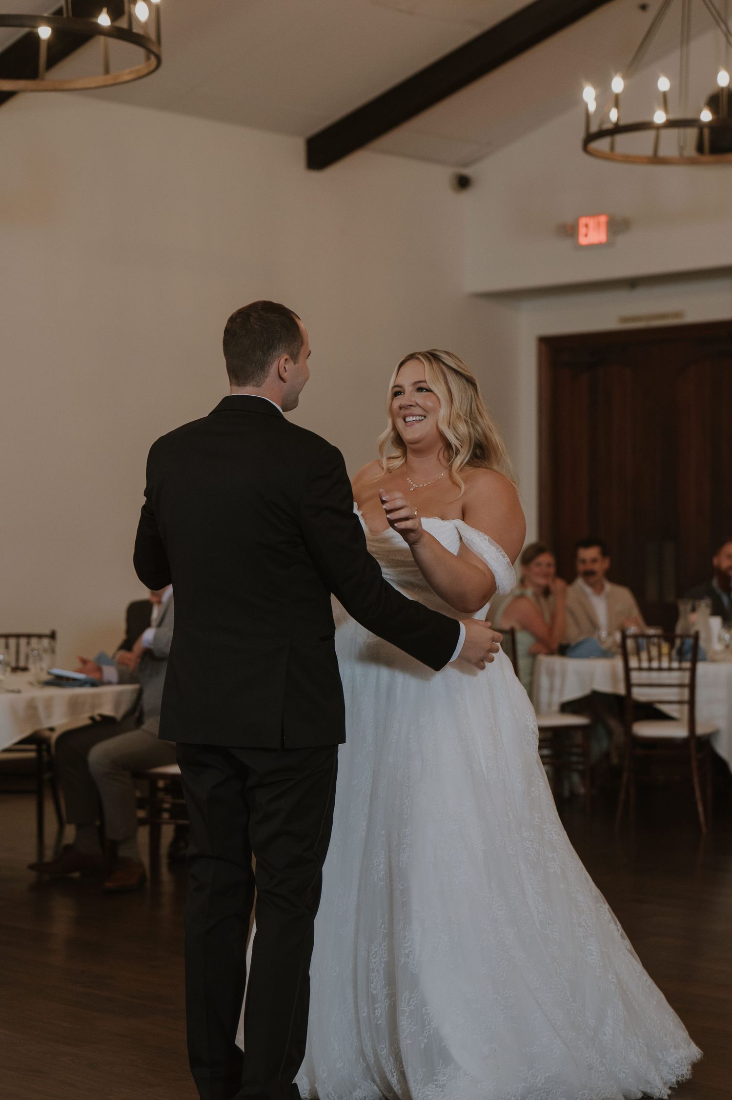 Bride in off-shoulder gown shares first dance with groom at elegant wedding reception.