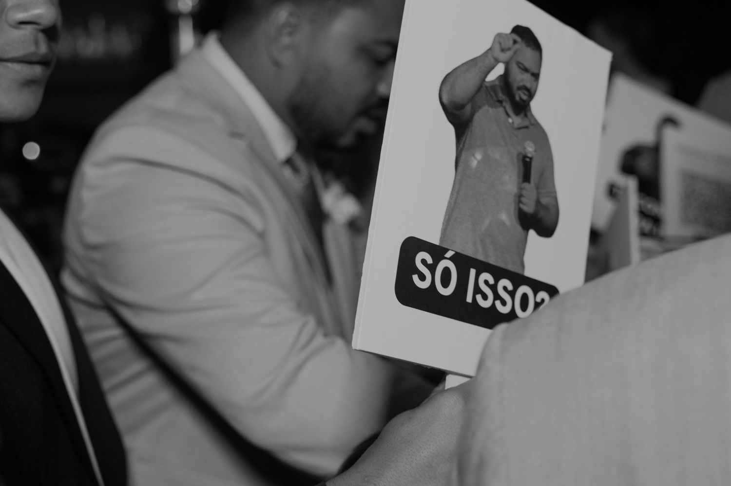 Black and white photo of a person holding a sign with a man's image and text reading SO ISSO at an event.