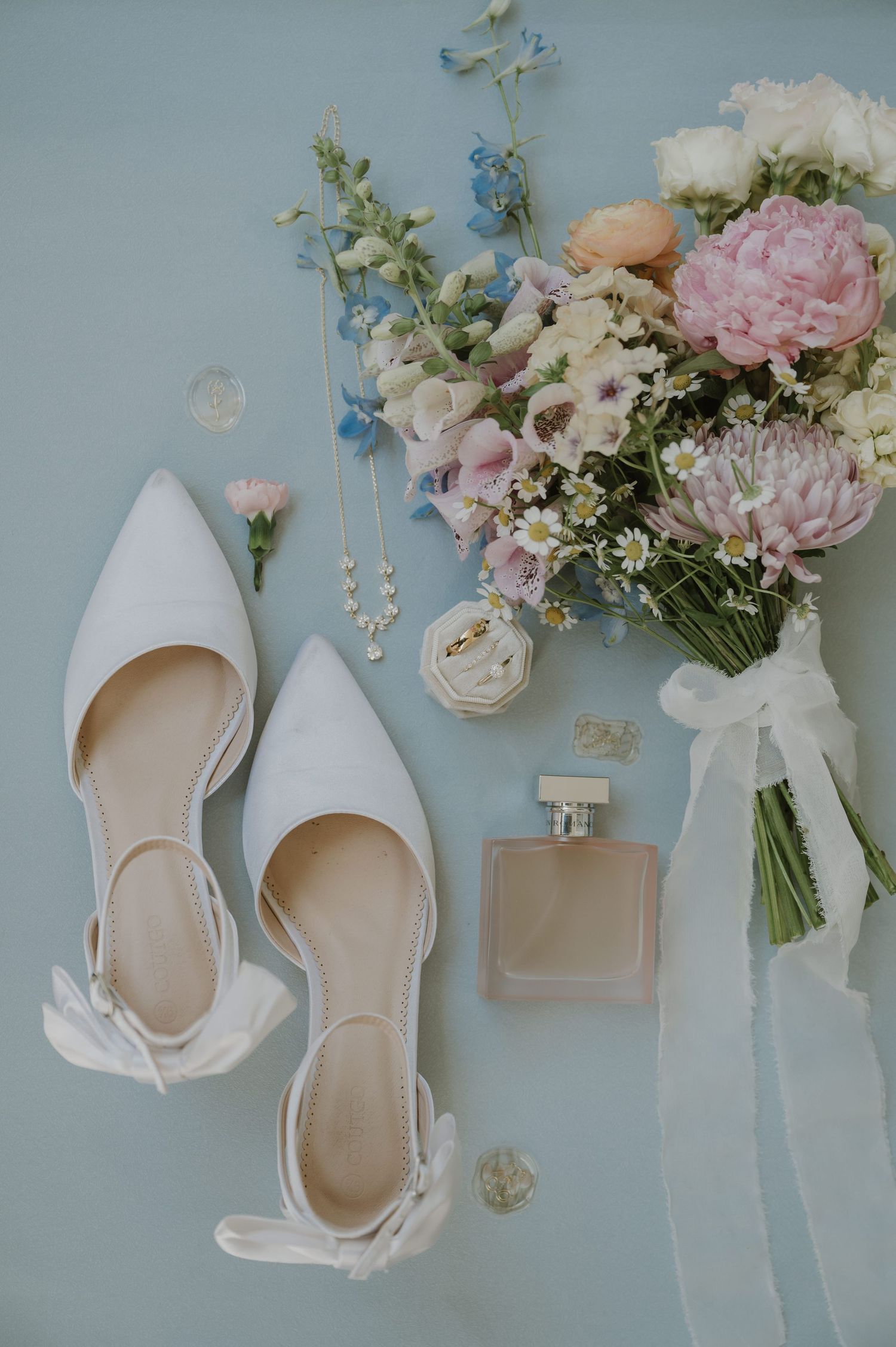 White bridal shoes and delicate pink floral arrangements on light blue background.