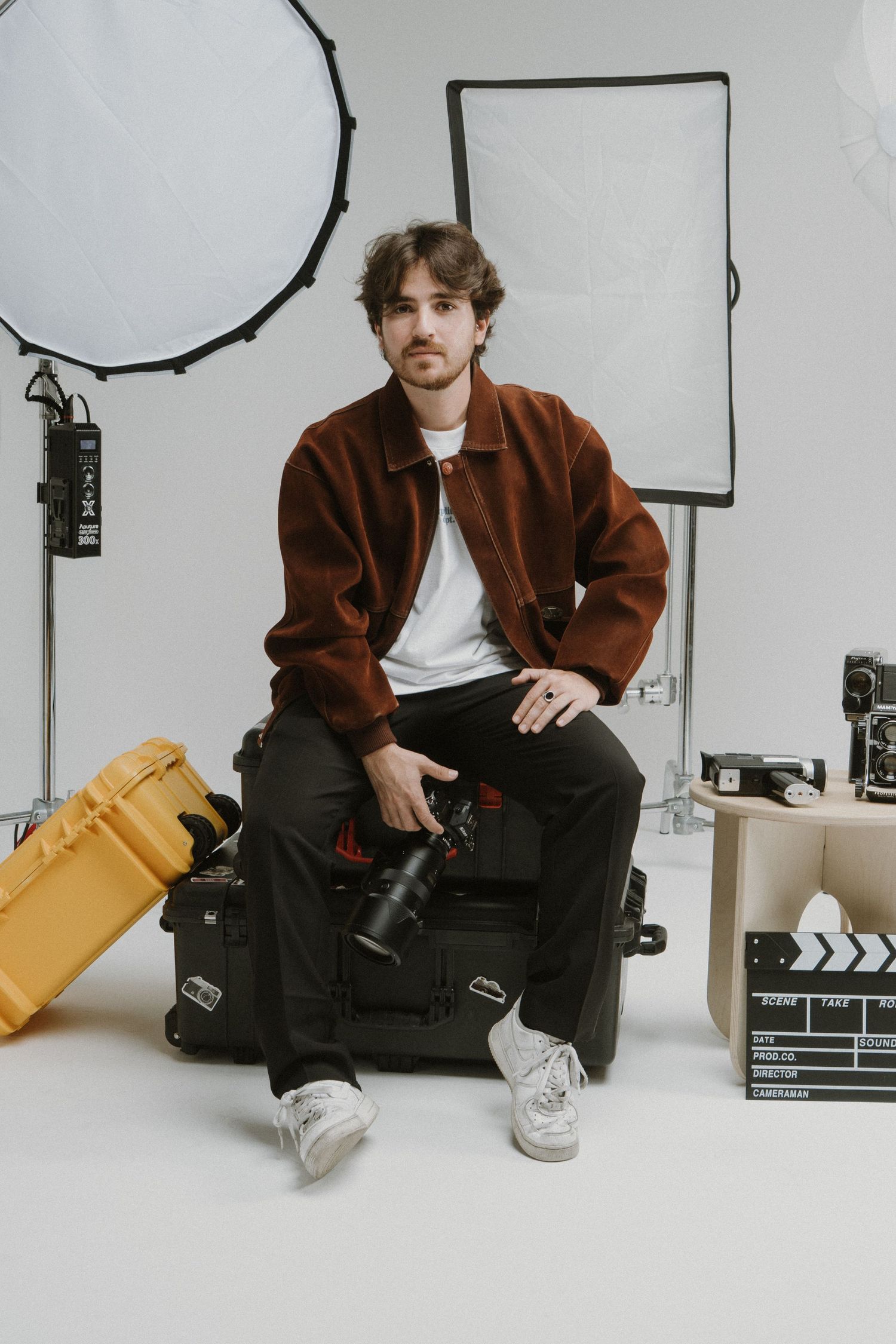 Behind-the-scenes photo showing film equipment and lighting setup in a studio with brown jacket and casual attire.
