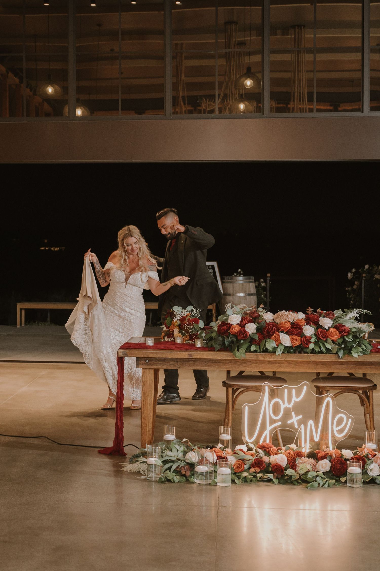 Wedding reception setup with floral arrangements and illuminated signage on rustic wooden tables.