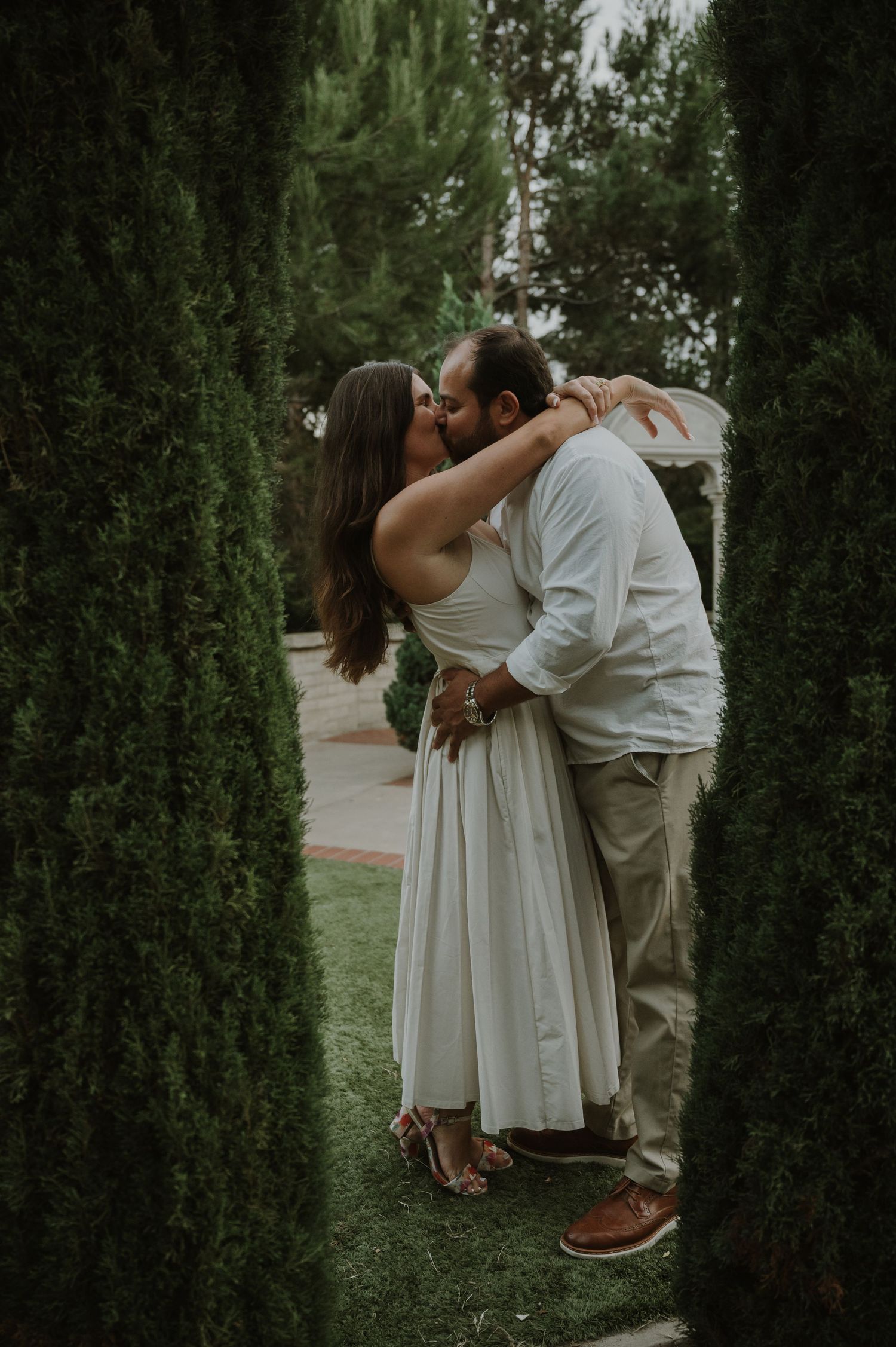 Intimate moment between couple among tall cypress trees in a garden setting.
