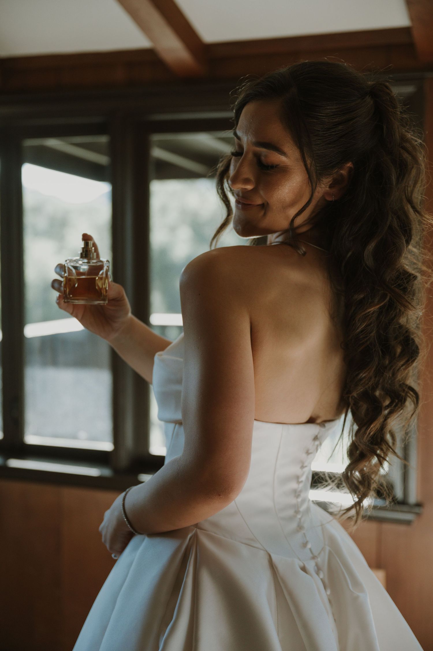 A bride in a white dress takes a sip from a glass during wedding preparations.