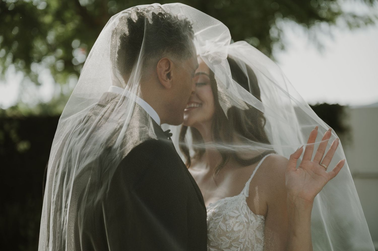 Bride and groom sharing a romantic moment under a flowing wedding veil outdoors.