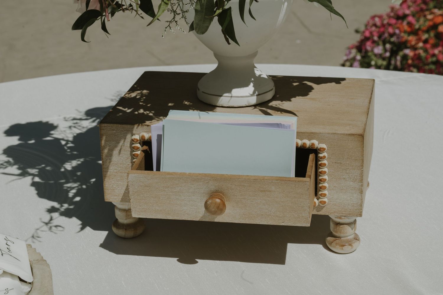 Rustic wooden card box with beaded details and small drawer, holding cards on a white table at an outdoor wedding.
