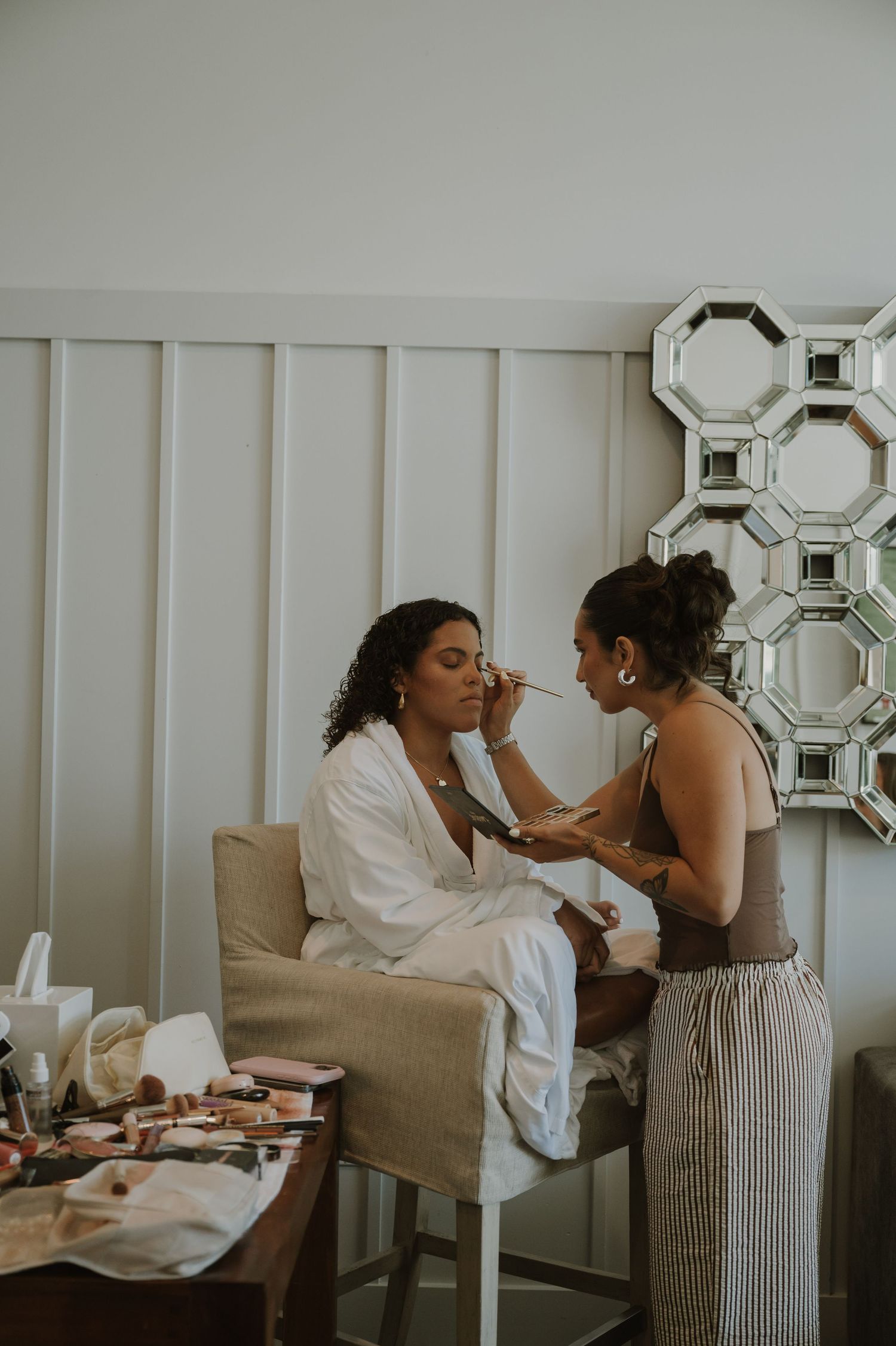 Makeup artist applying foundation to a bride in a white robe during wedding preparations.