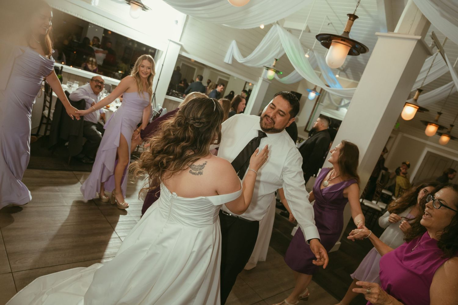 Bride and groom share energetic dance at wedding reception surrounded by celebrating guests.