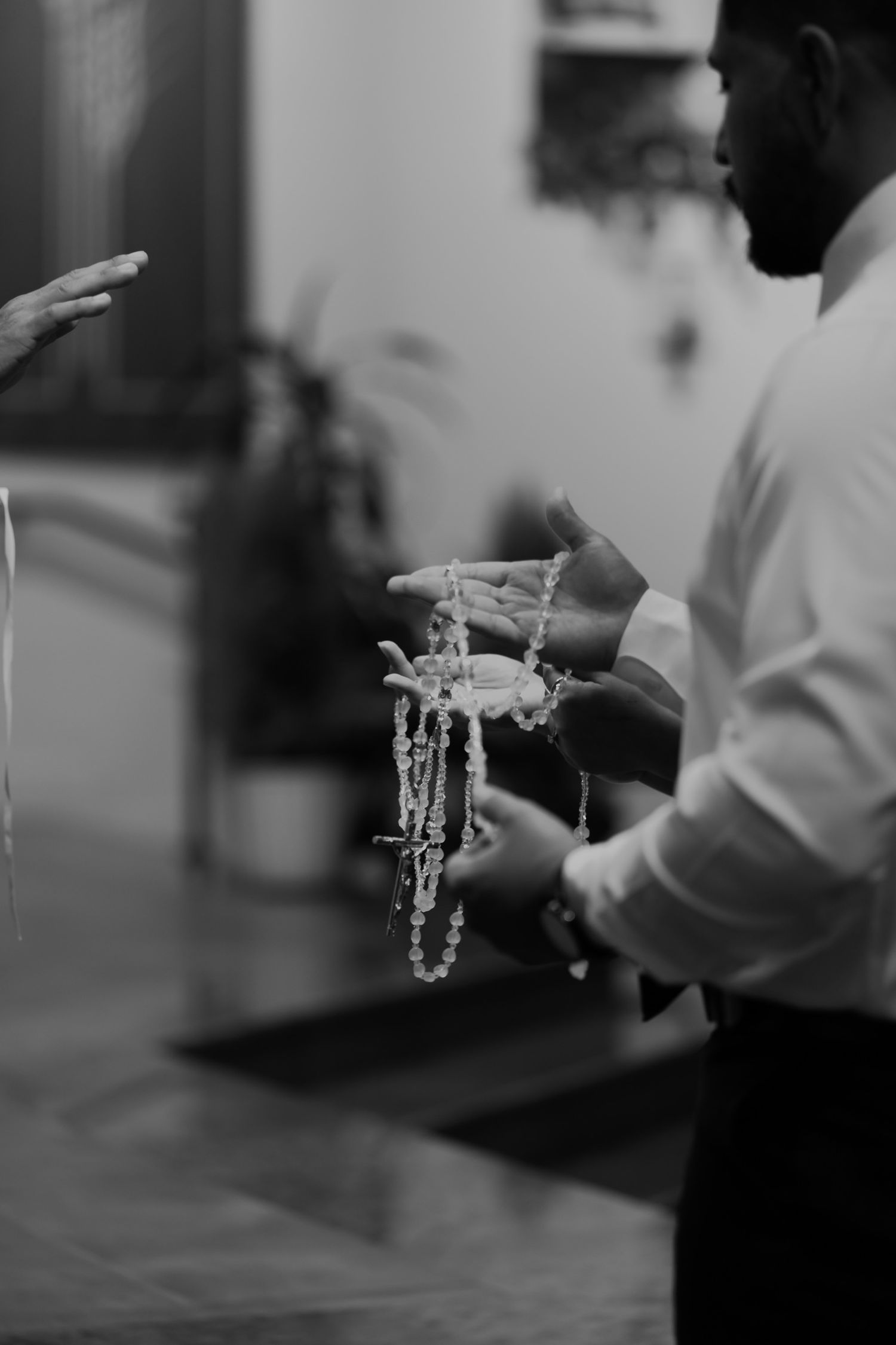 Black and white photo of a man holding rosary beads during a religious ceremony.