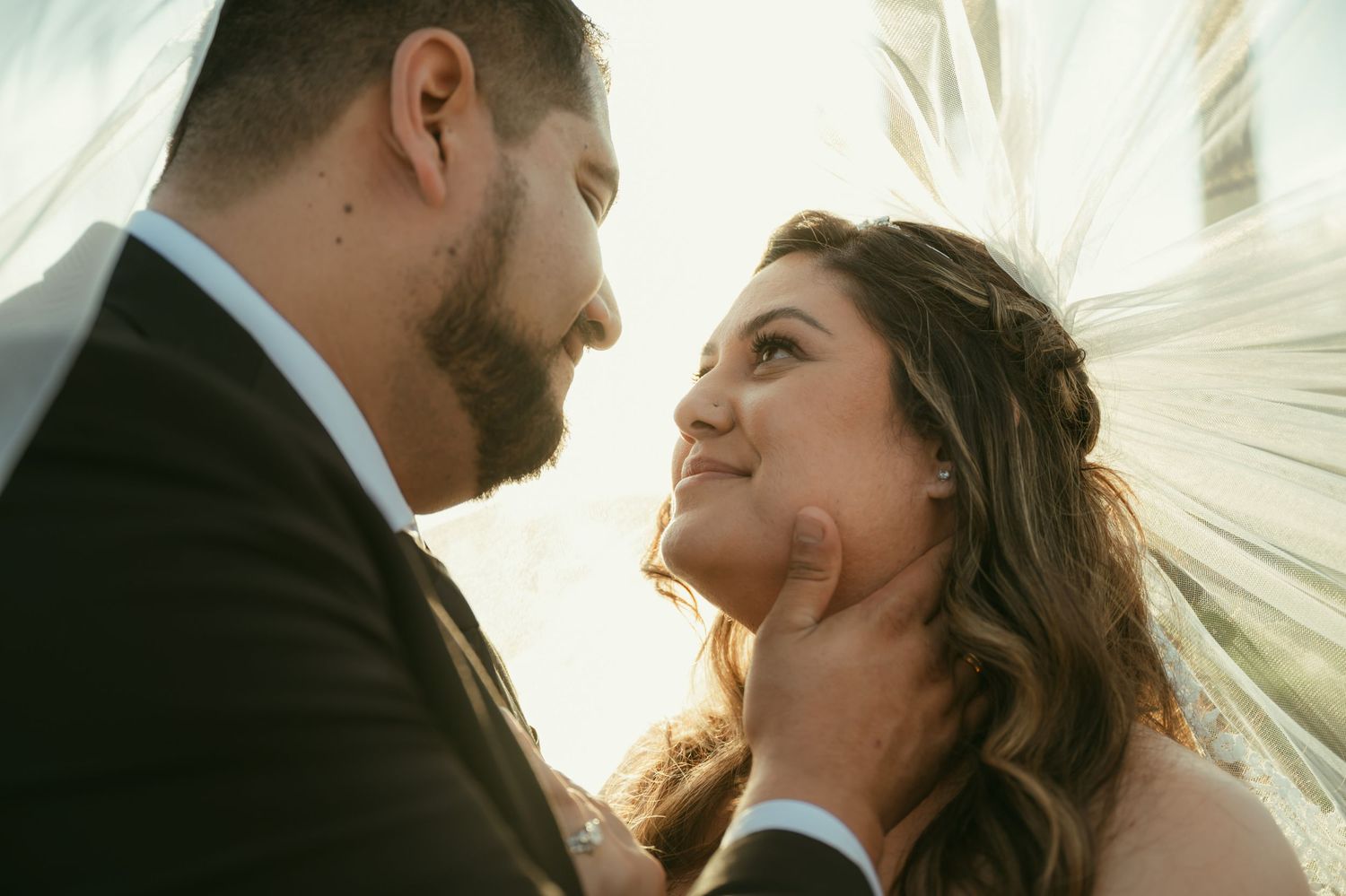 Romantic wedding couple sharing an intimate moment, groom tenderly holding bride's face under a flowing veil.