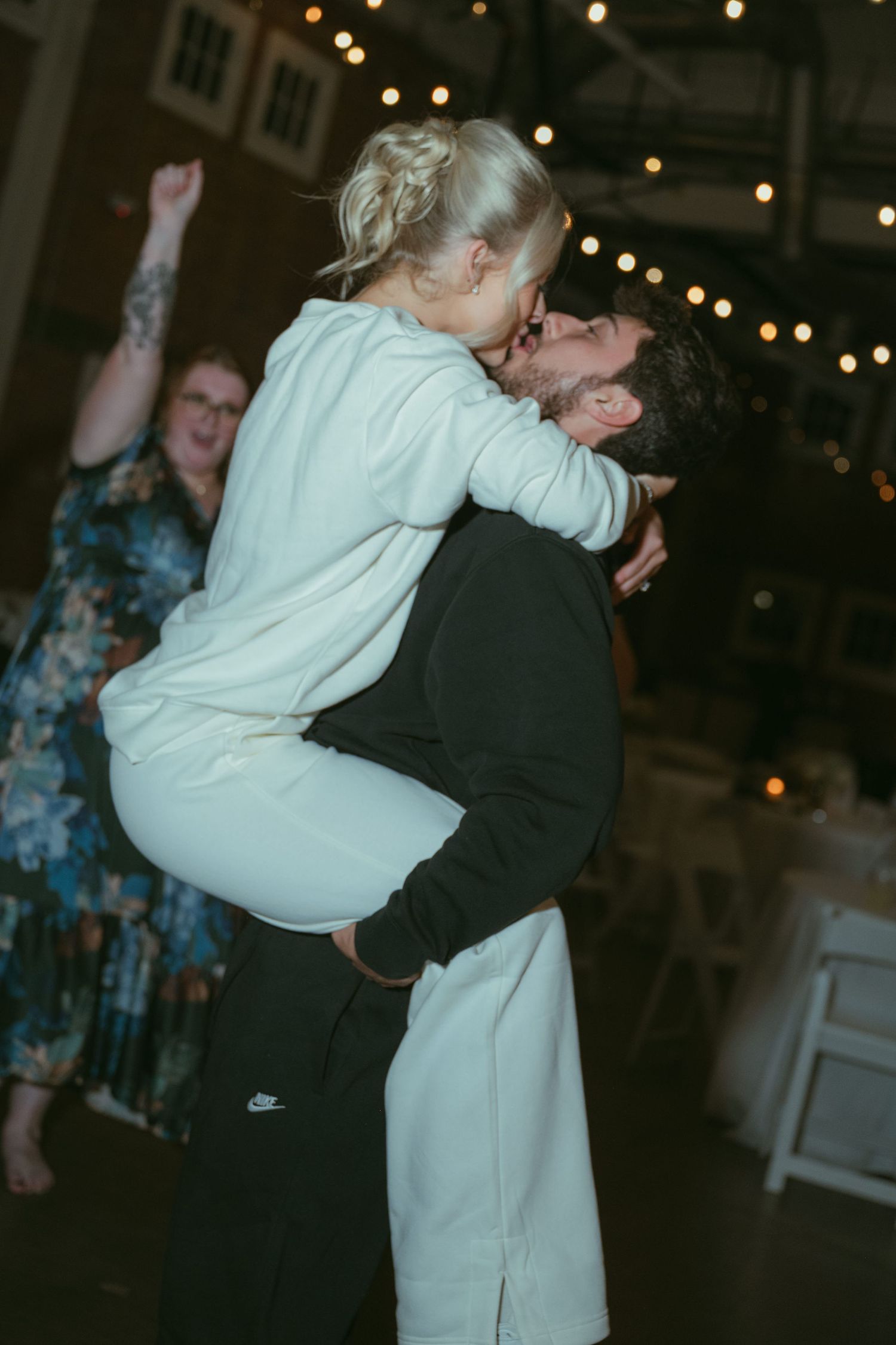 Groom lifting and kissing bride in casual attire on wedding reception dance floor.