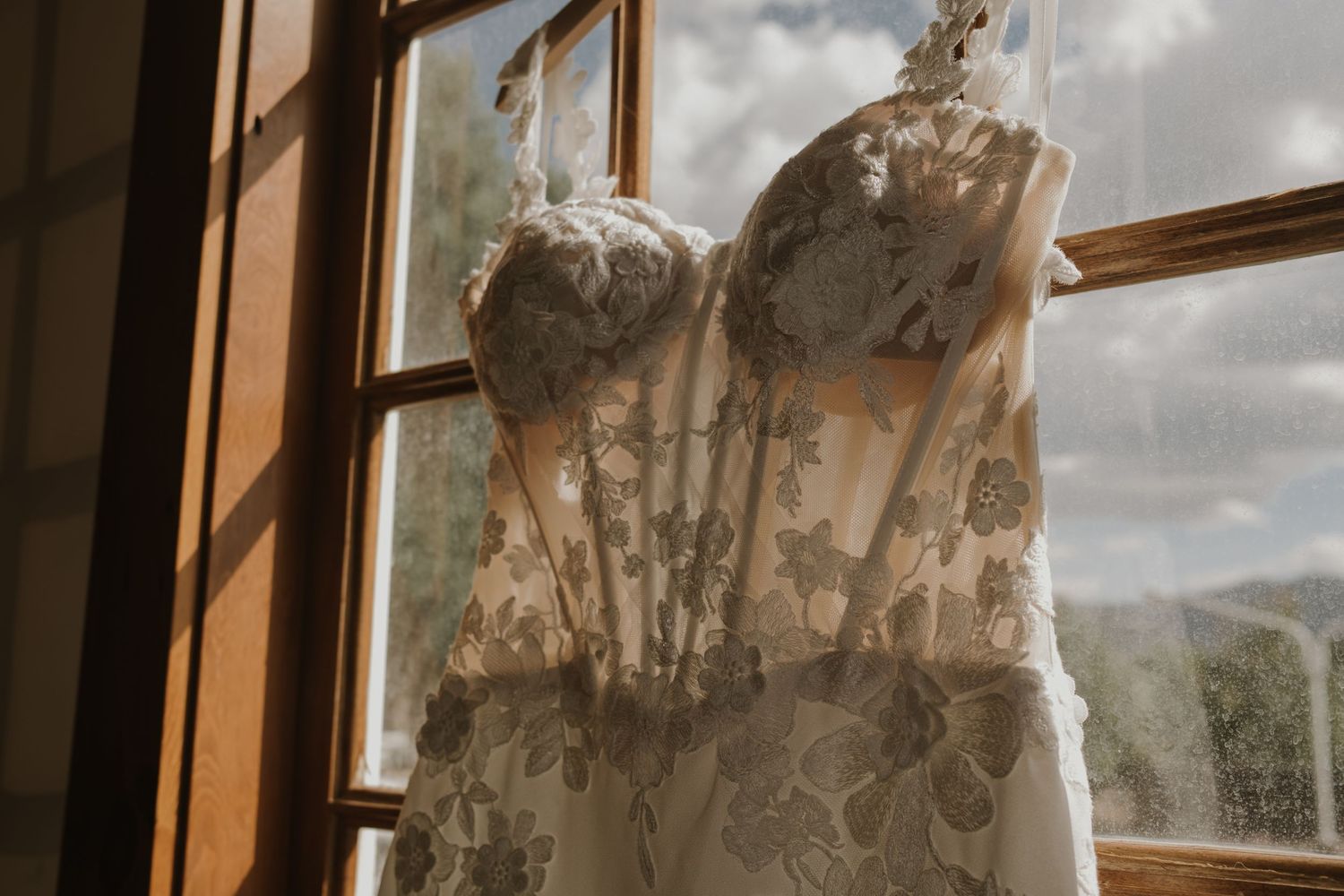 Wedding dress hanging by window with dramatic natural lighting and mountain view.