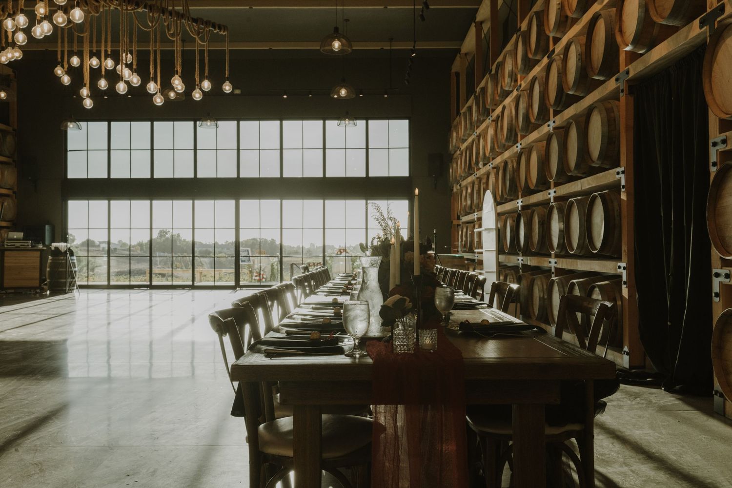 Industrial winery interior with dramatic lighting and rows of stacked barrels along the walls.