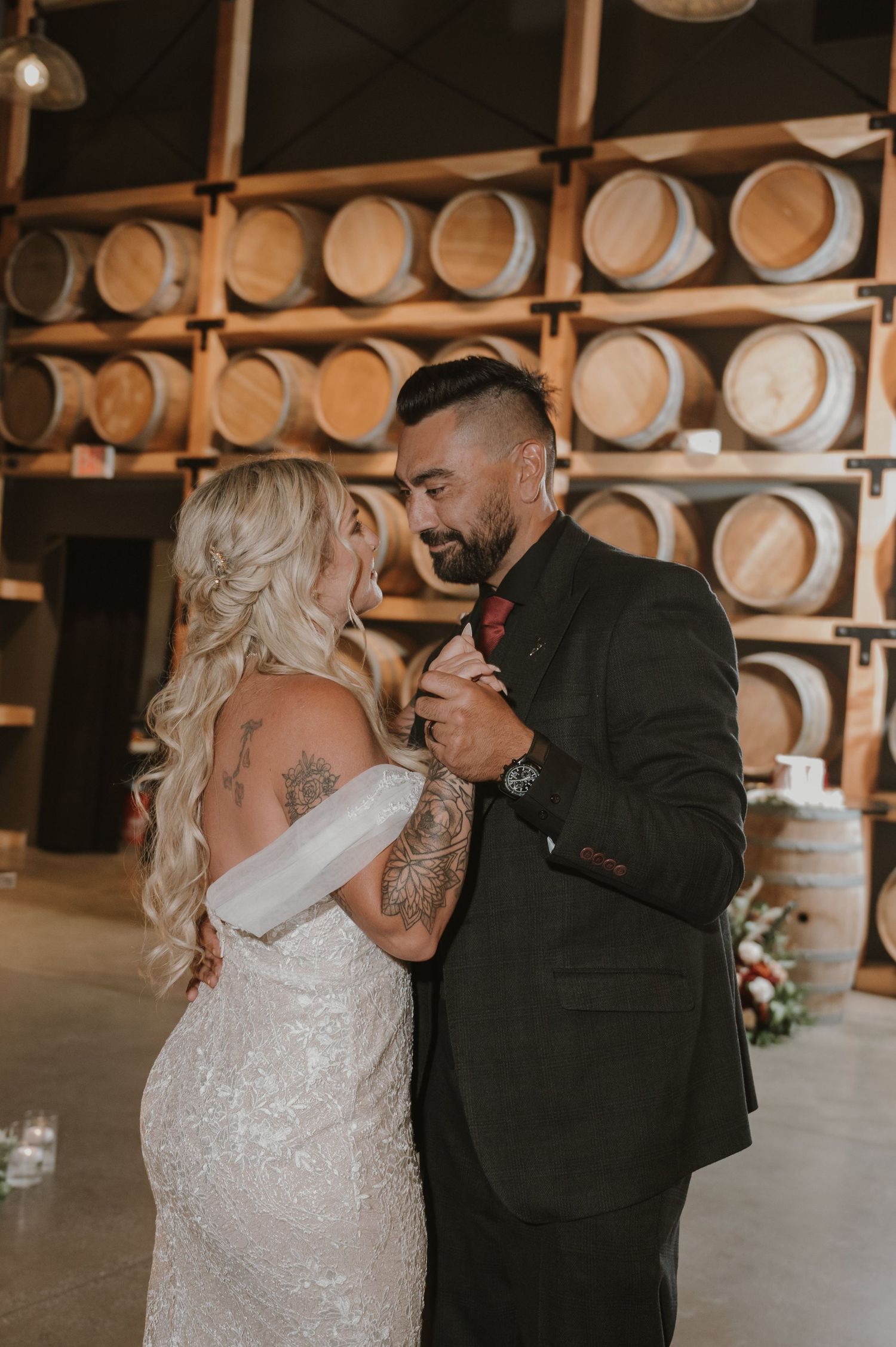 Wedding couple shares intimate moment in front of rustic wine barrel wall.