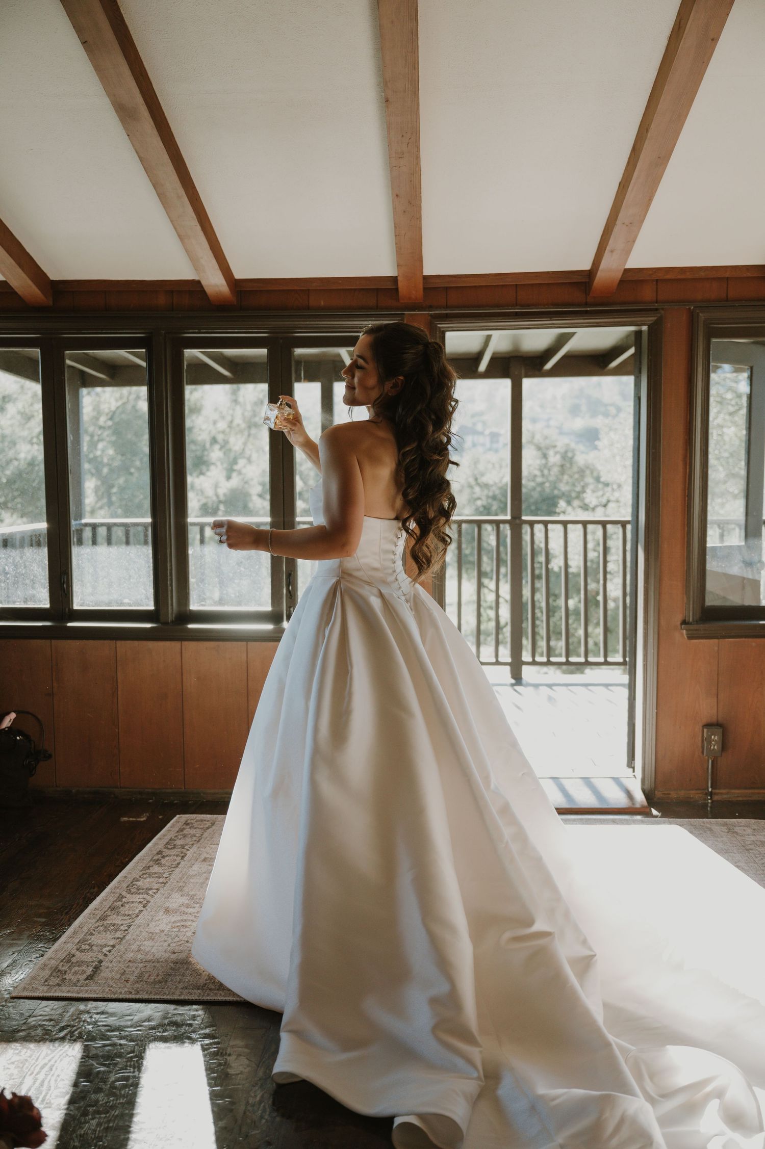 A wedding dress with a dramatic train photographed in a rustic room with wooden beams and windows.