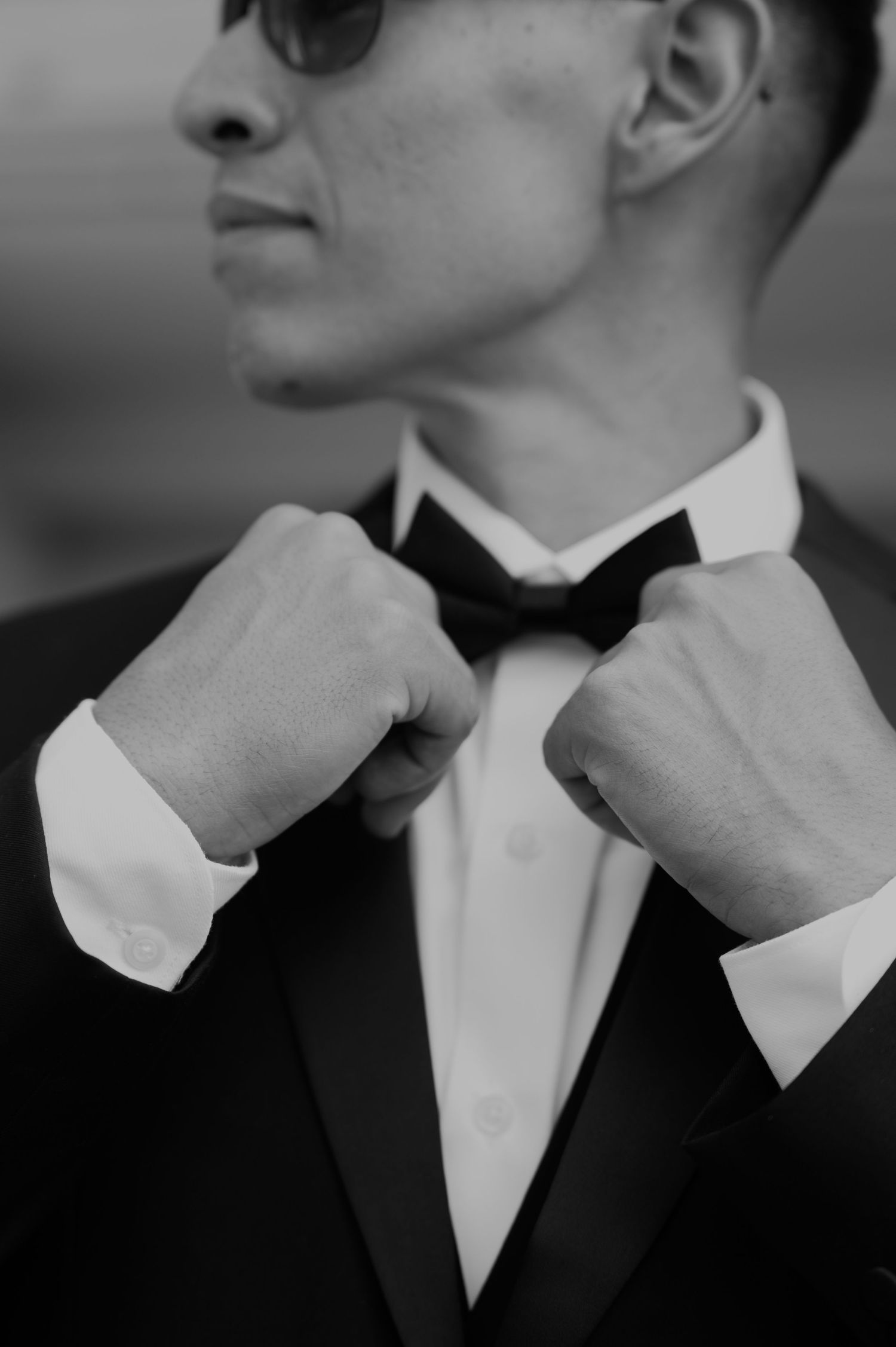 Close-up black and white photo of hands adjusting bow tie on formal tuxedo.