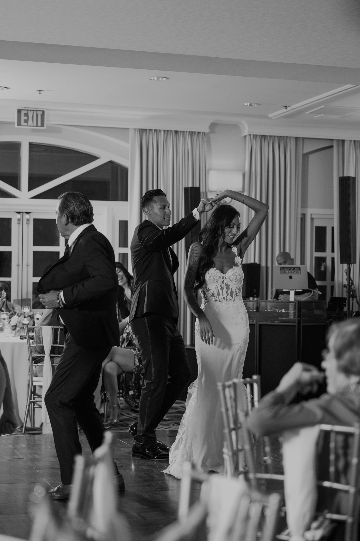 Black and white photo of wedding guests dancing in synchronized moves at reception.