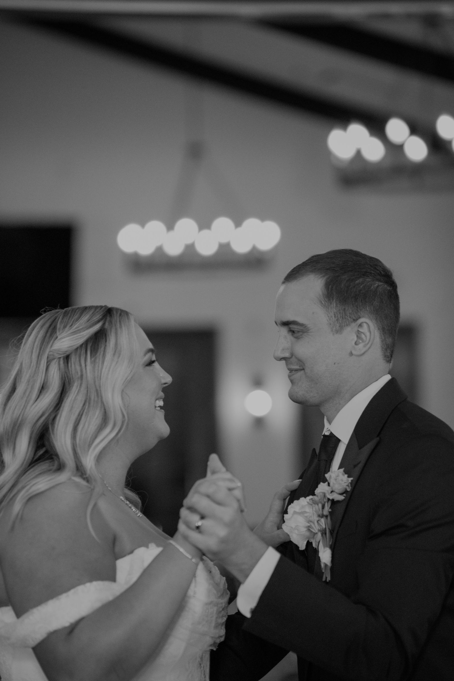 Black and white photo of bride and groom sharing their first dance, smiling joyfully at each other.