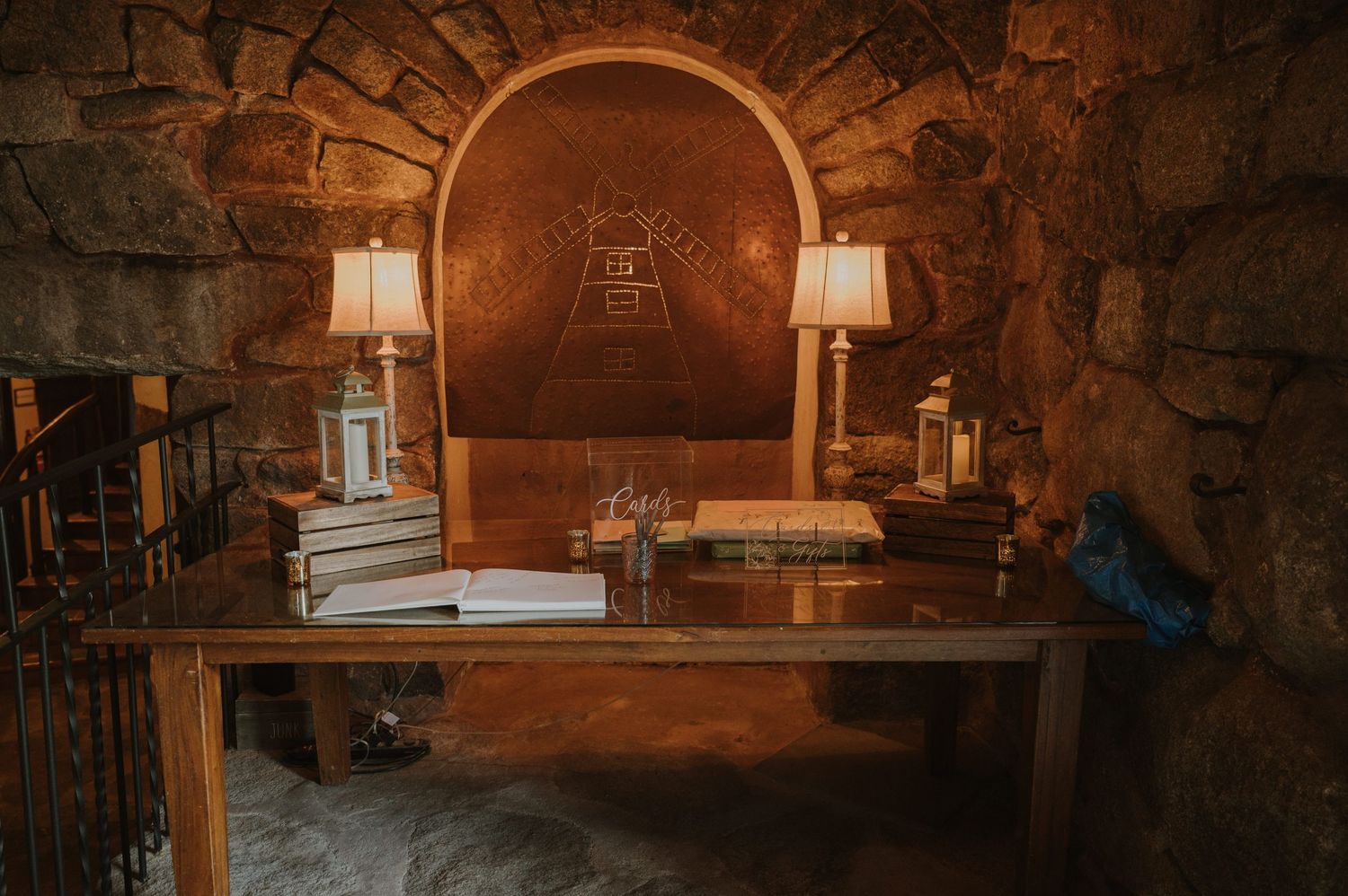 Rustic stone wine cellar with wooden table, lamps, and arched copper wall accent.