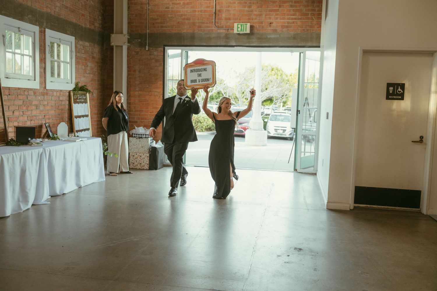 Couple makes grand entrance at wedding reception in industrial venue with brick walls and open garage door.