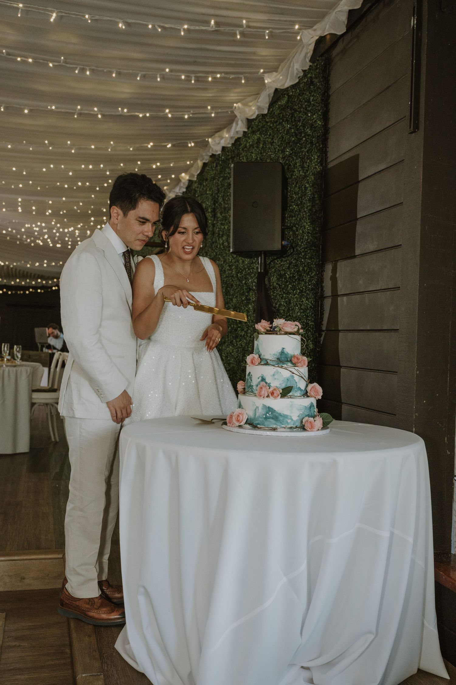 Bride and groom cutting three-tier marble wedding cake decorated with pink roses at reception.