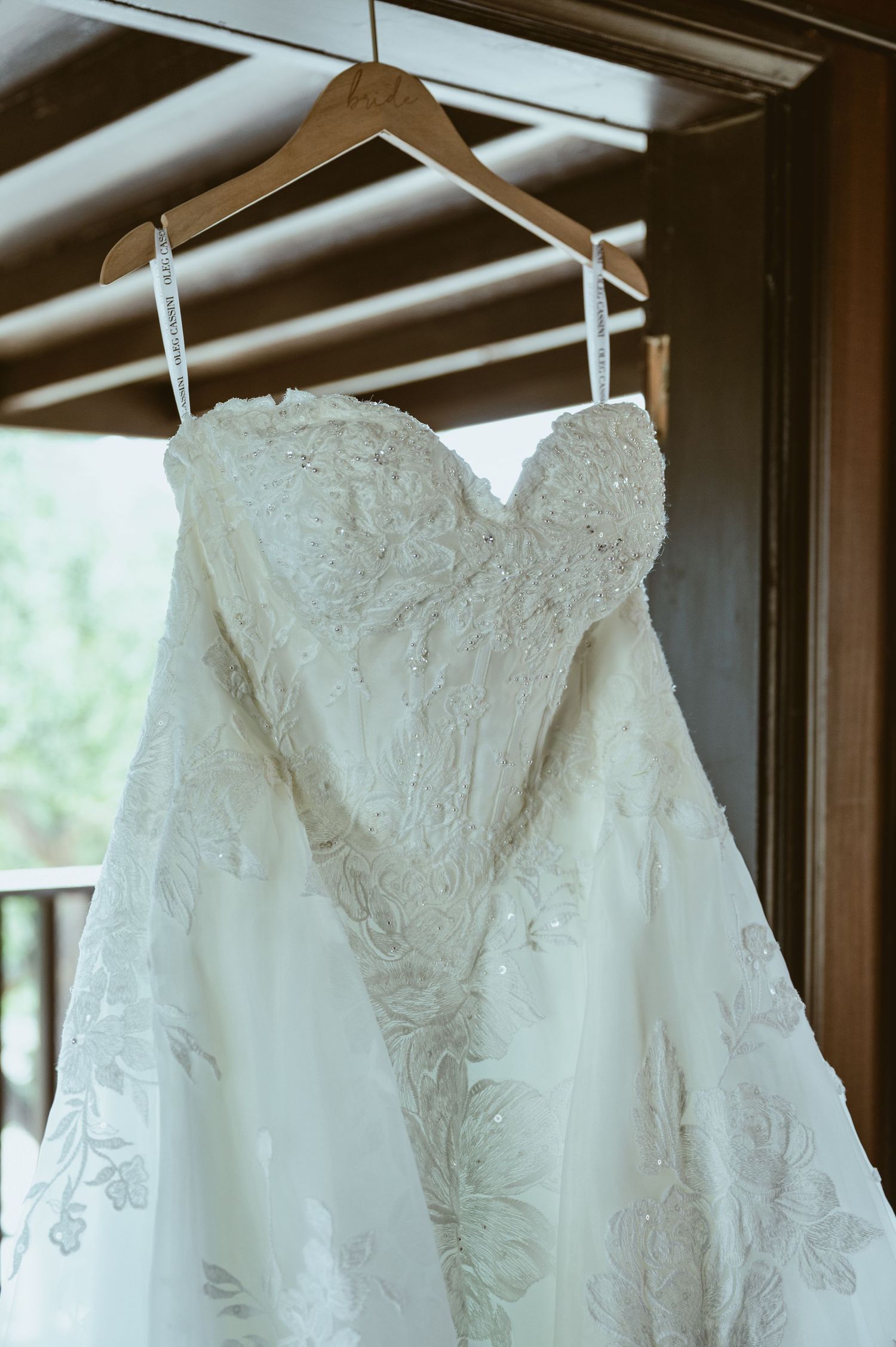 Elegant strapless lace wedding gown hanging on a wooden hanger in a rustic venue with natural light.