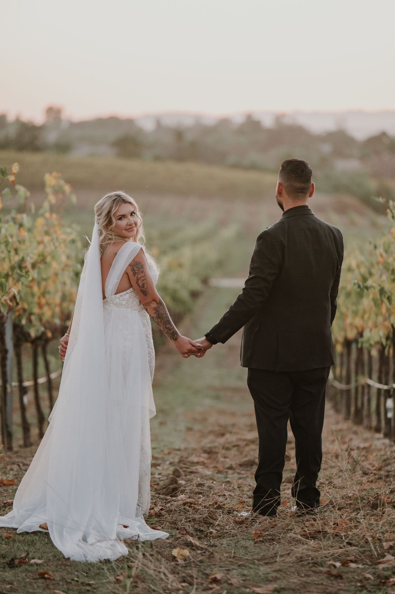 Couple walking through vineyard rows during golden hour wedding photography.