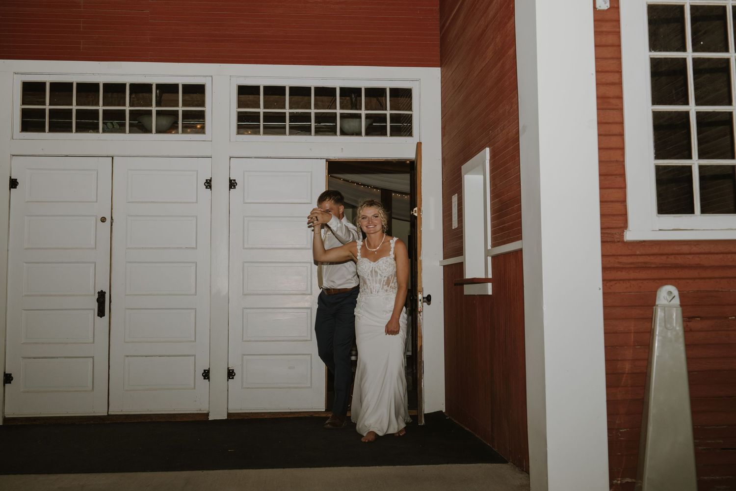 Red barn-style building with white trim and multiple doors creates a rustic wedding venue backdrop.