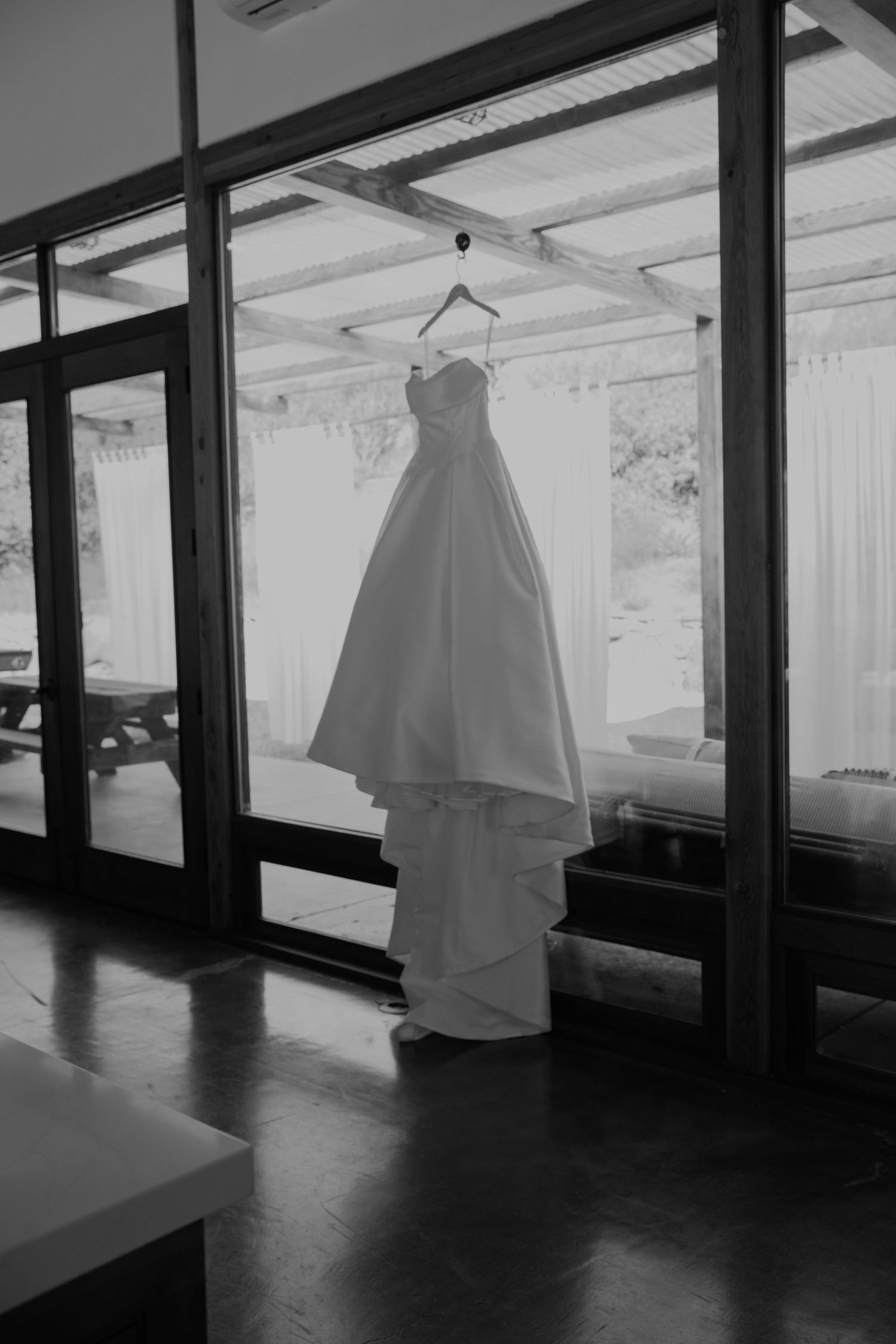 Wedding dress hanging in window with dramatic natural lighting.