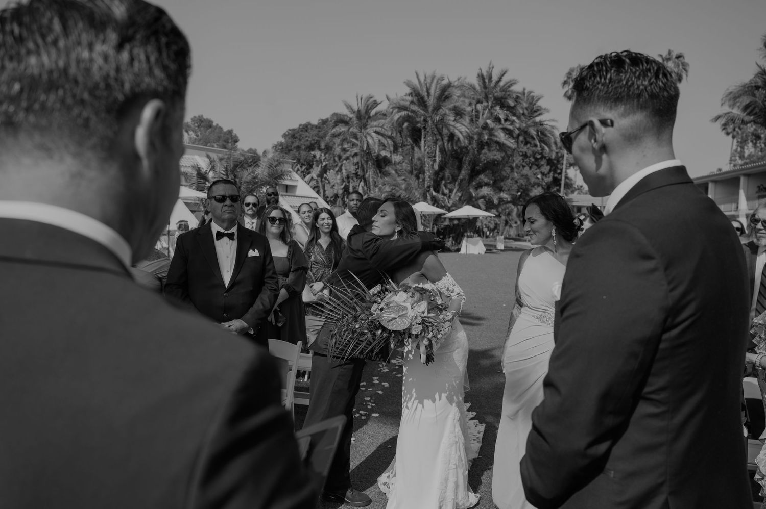 Black and white photo of an outdoor wedding ceremony with palm trees framing the scene.