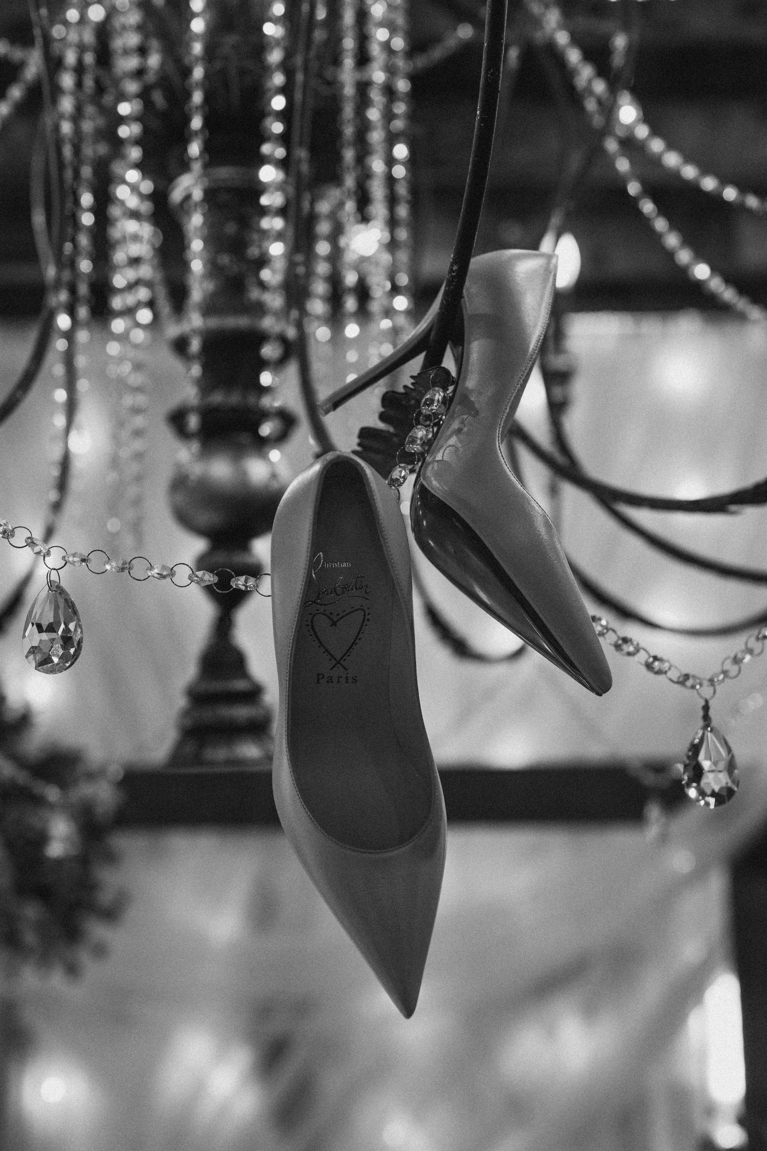 Black and white photo of elegant stiletto heels hanging from a chandelier with crystal decorations.