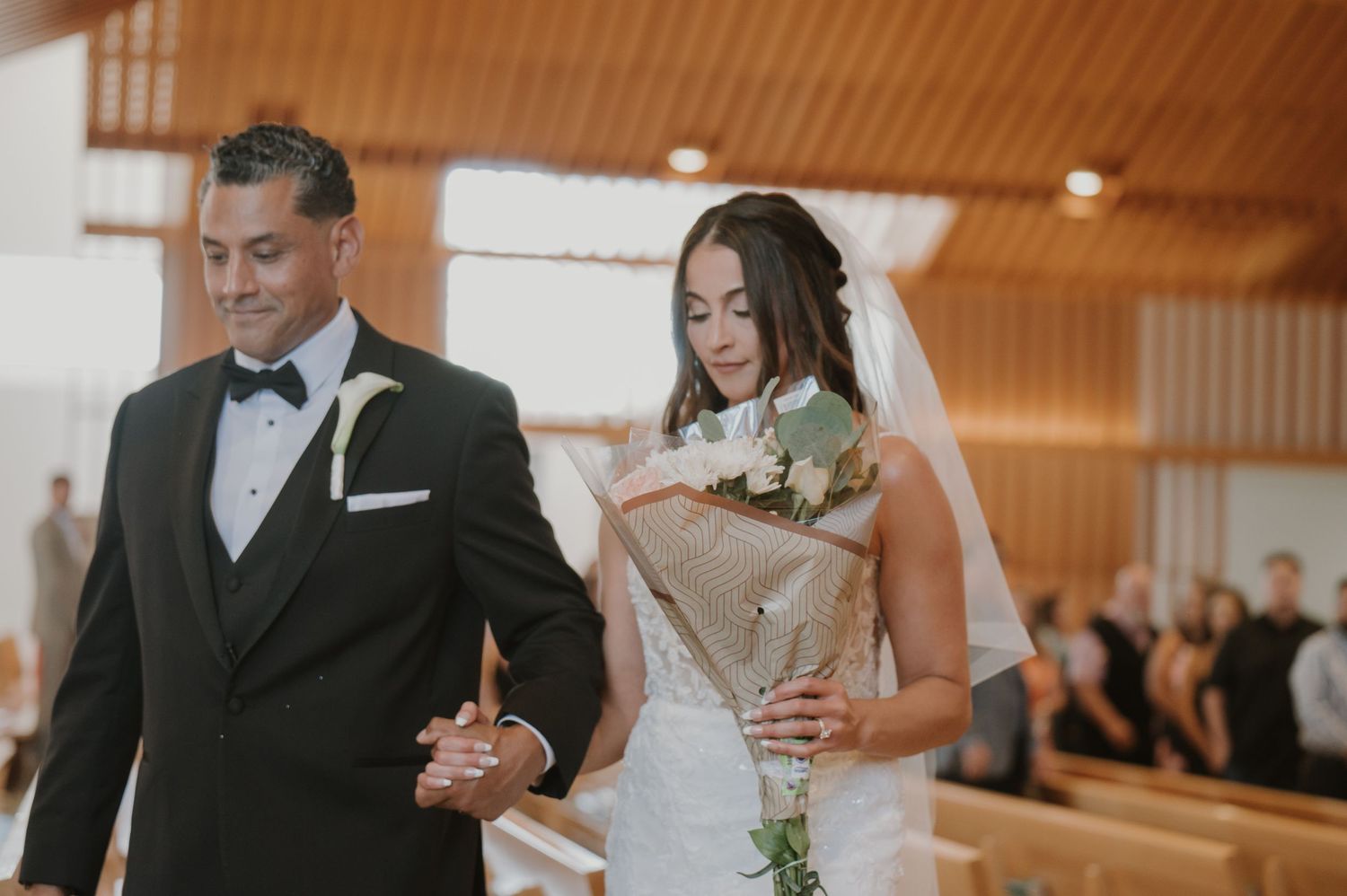 Bride and groom walking down church aisle together, bride holding bouquet, groom in black tuxedo, wedding ceremony.