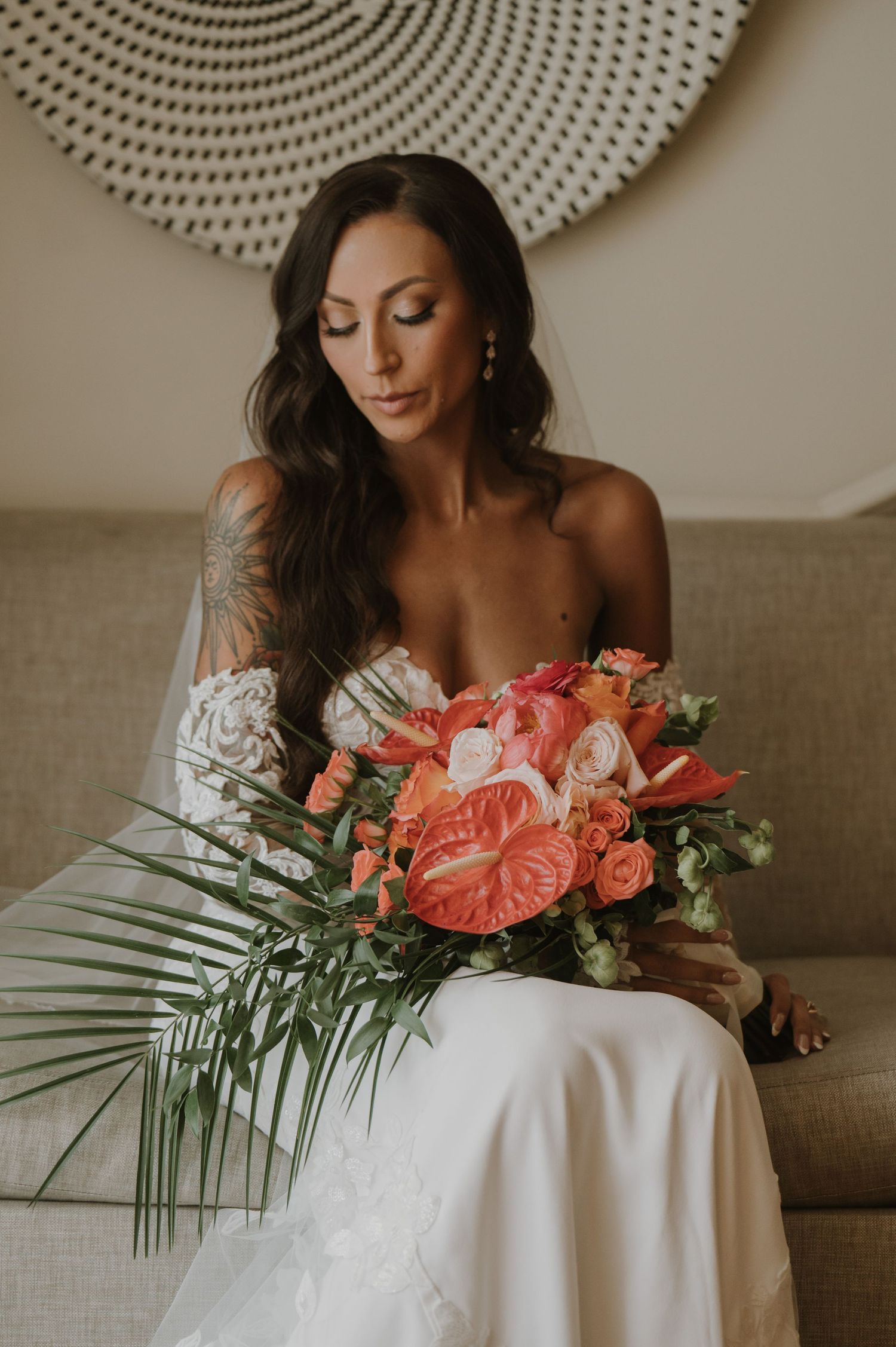 Tropical wedding bouquet with coral anthuriums and palm leaves on white fabric.