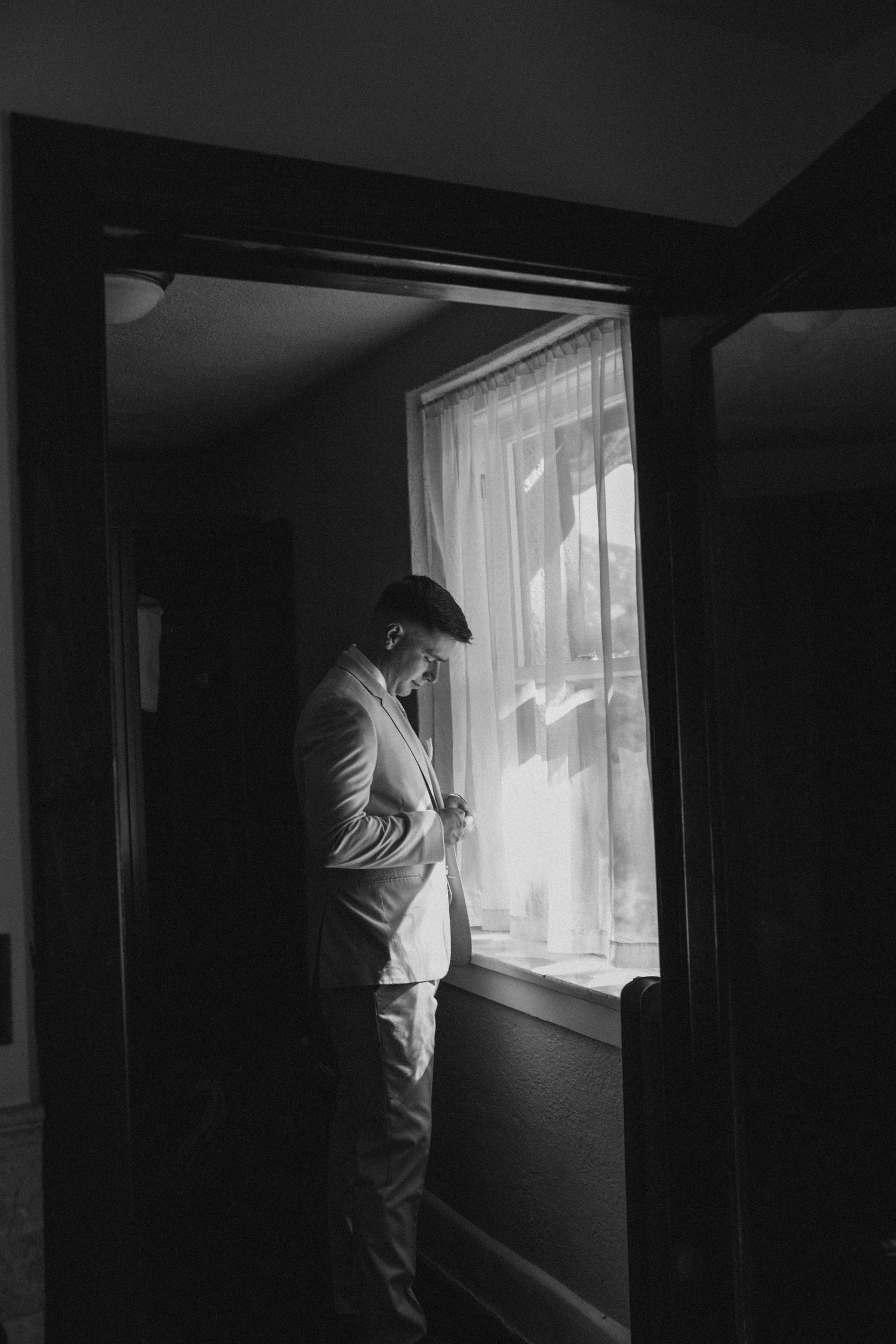 Black and white photos of person gazing through bright window in dark room.