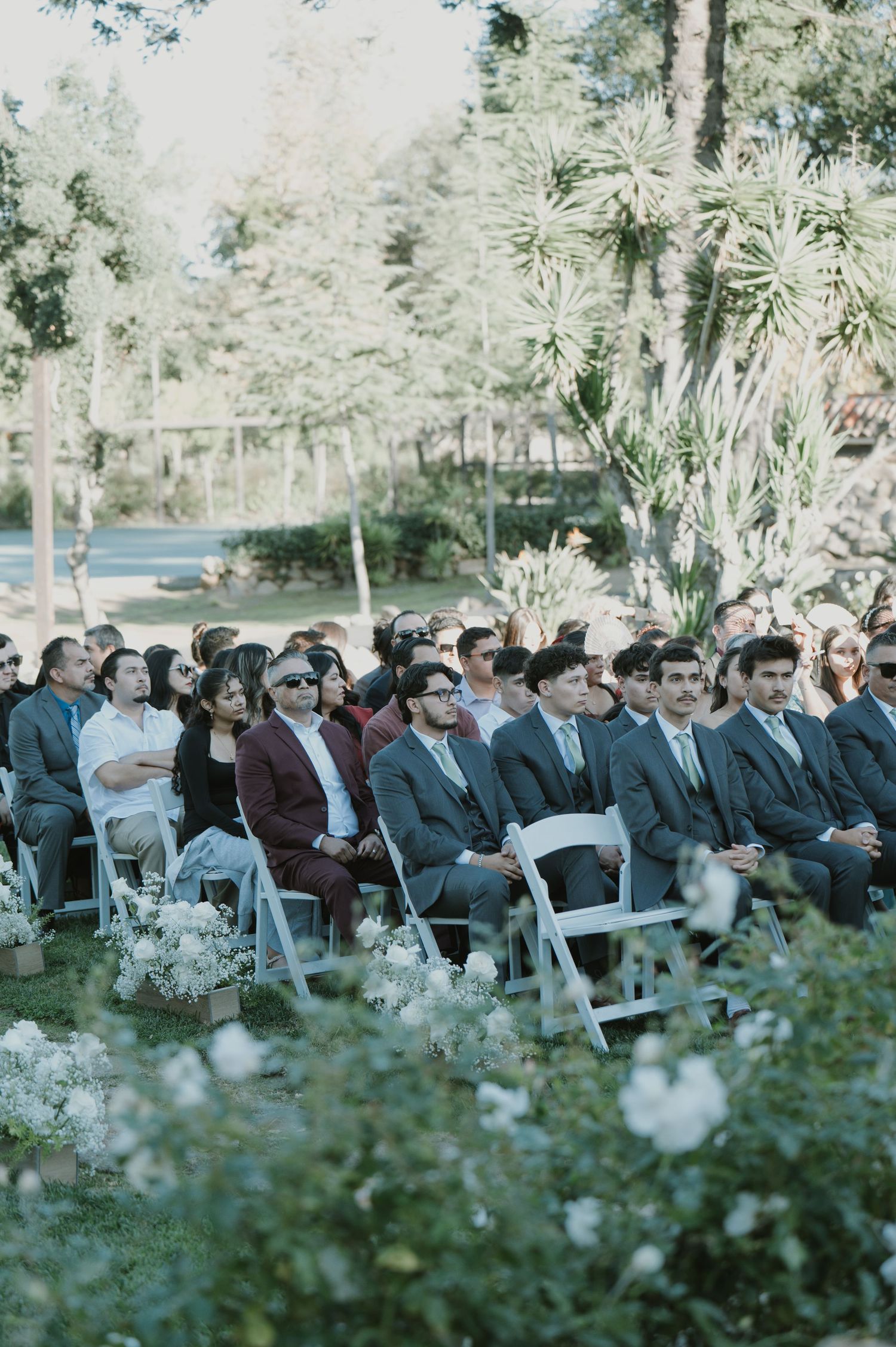 Outdoor wedding ceremony with guests seated in white chairs among garden flowers.