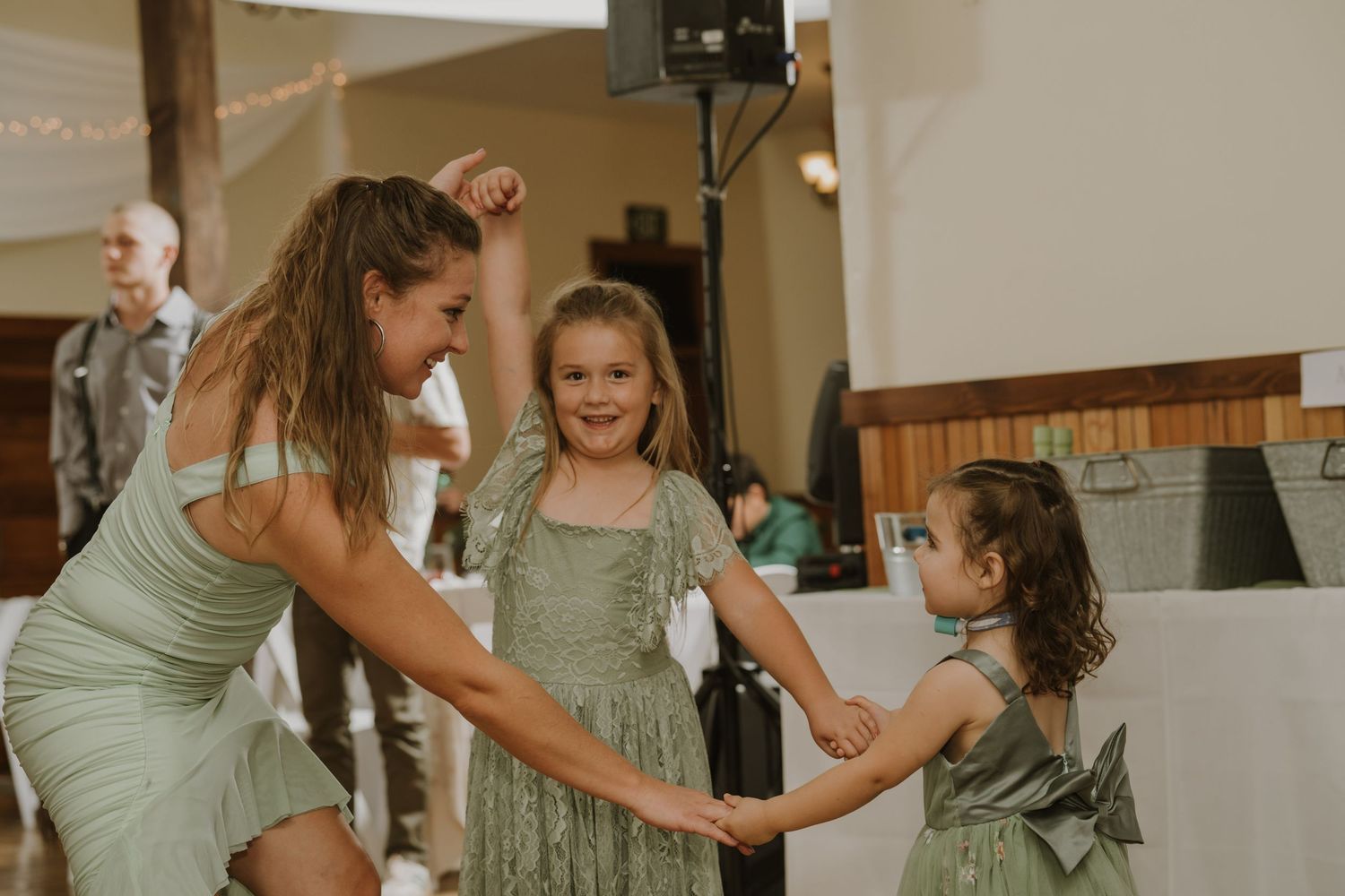Wedding party members in sage green dresses dancing together at a reception.