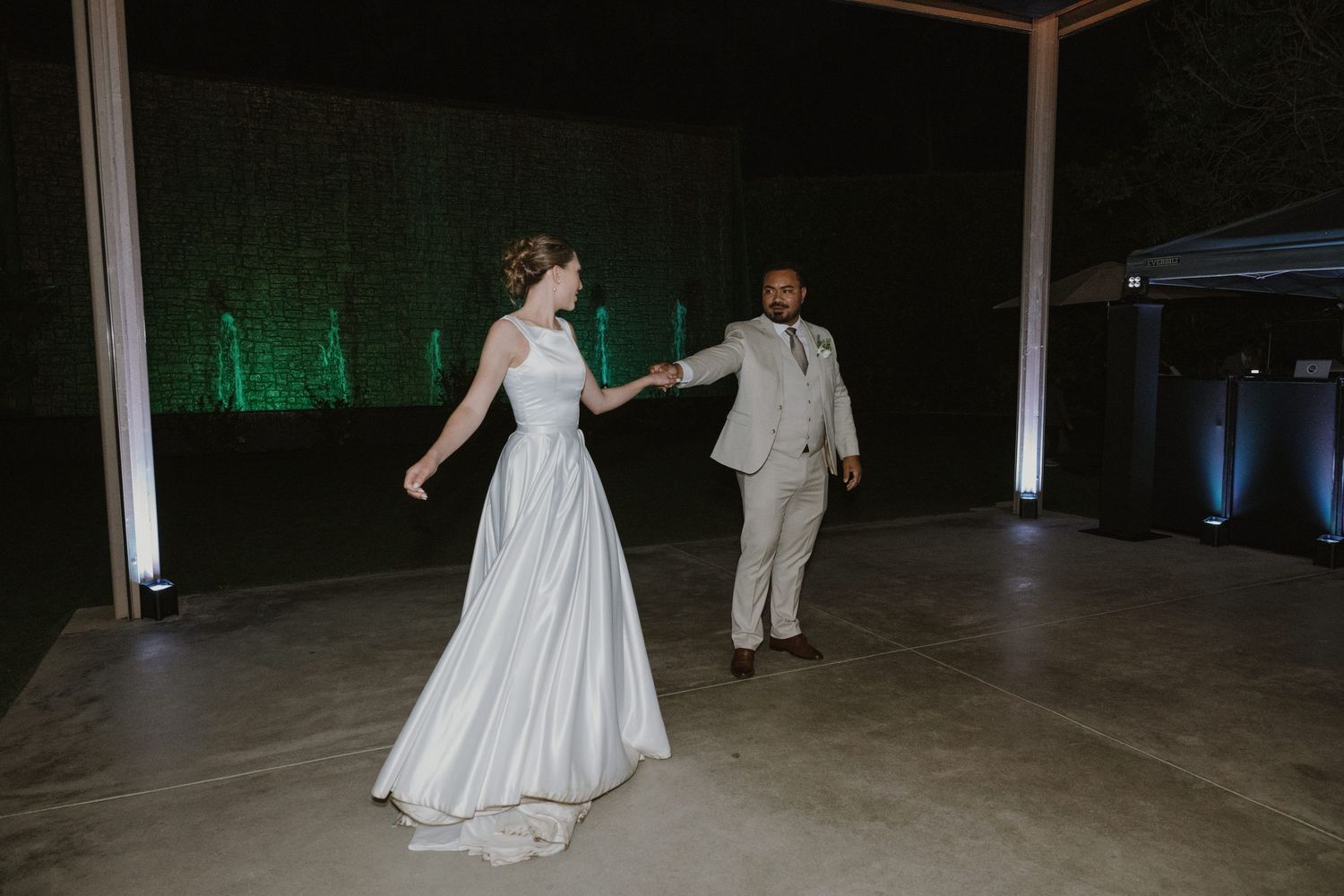 Bride and groom share first dance on outdoor dance floor with green uplighting at evening wedding reception.