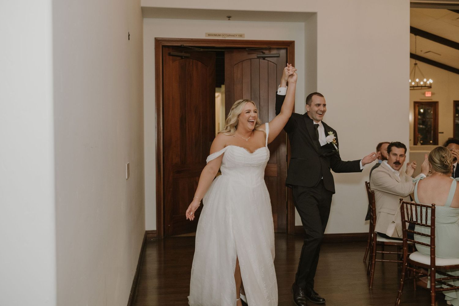 Joyful bride and groom making grand entrance into wedding reception with hands raised.