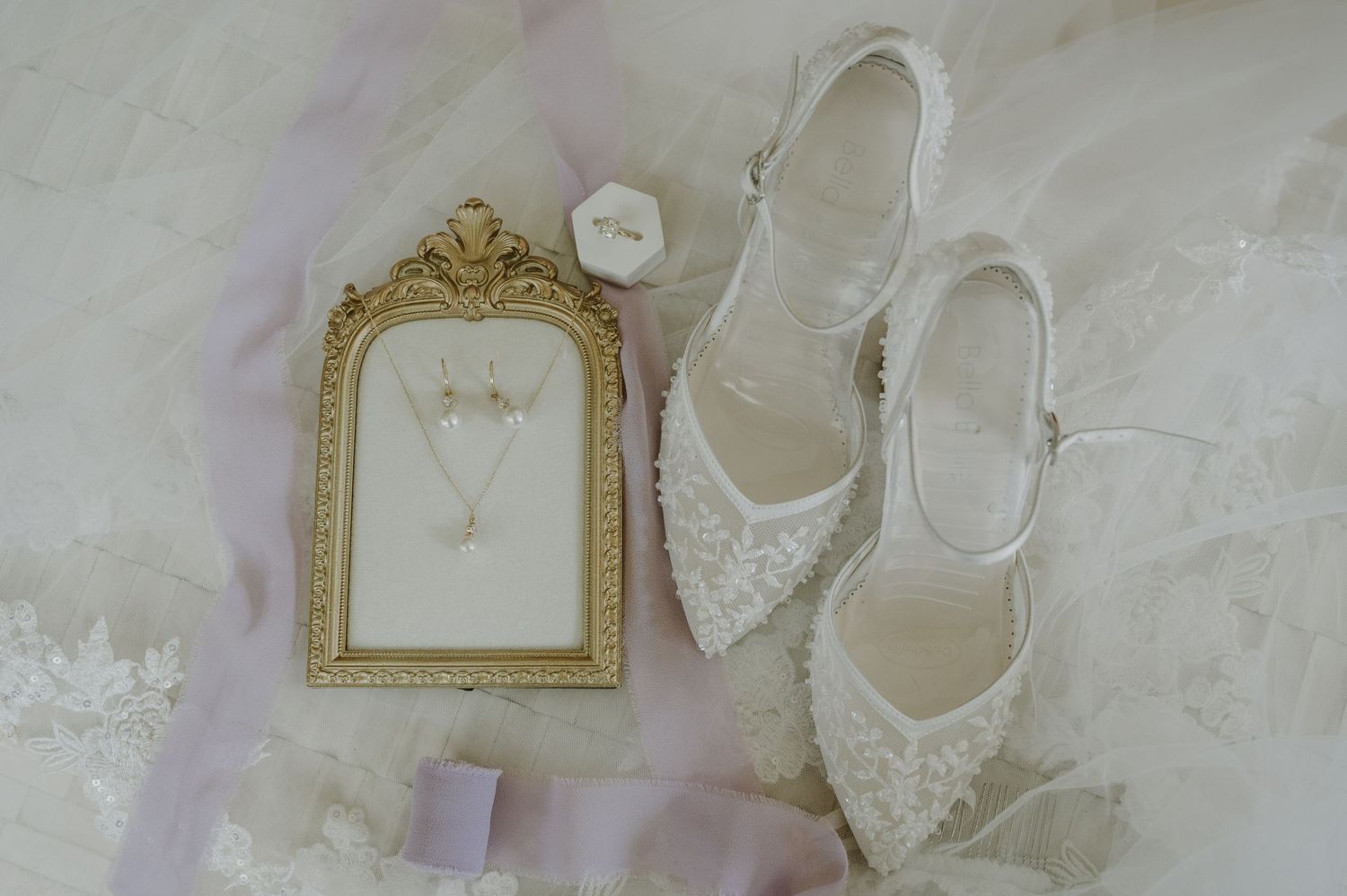 Bridal accessories flat lay featuring white lace heels, gold framed jewelry display, pearl necklace, and earrings on marble.