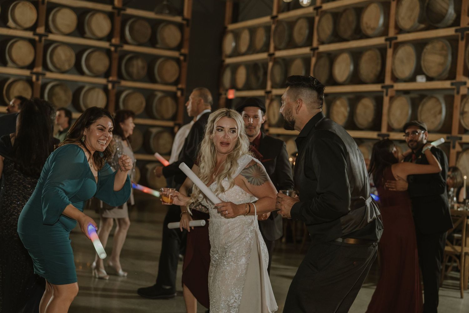 Wedding party dancing and celebrating in rustic venue with wooden barrel decor.