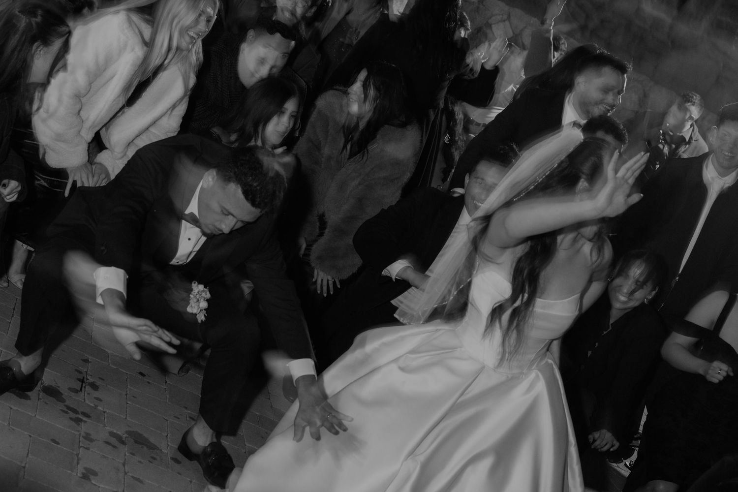 Black and white photo of wedding guests dancing energetically at a reception.