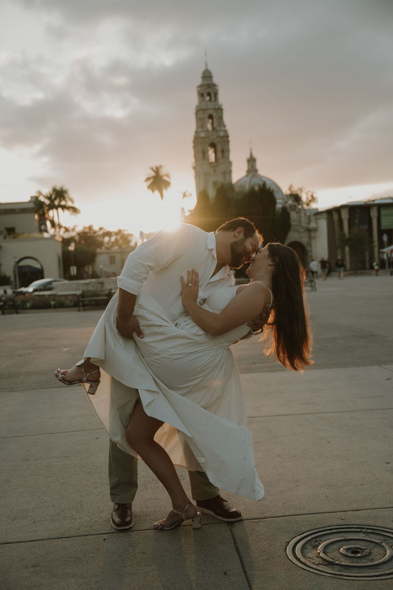 Couple dancing in a romantic dip pose at sunset in front of a historic church plaza.