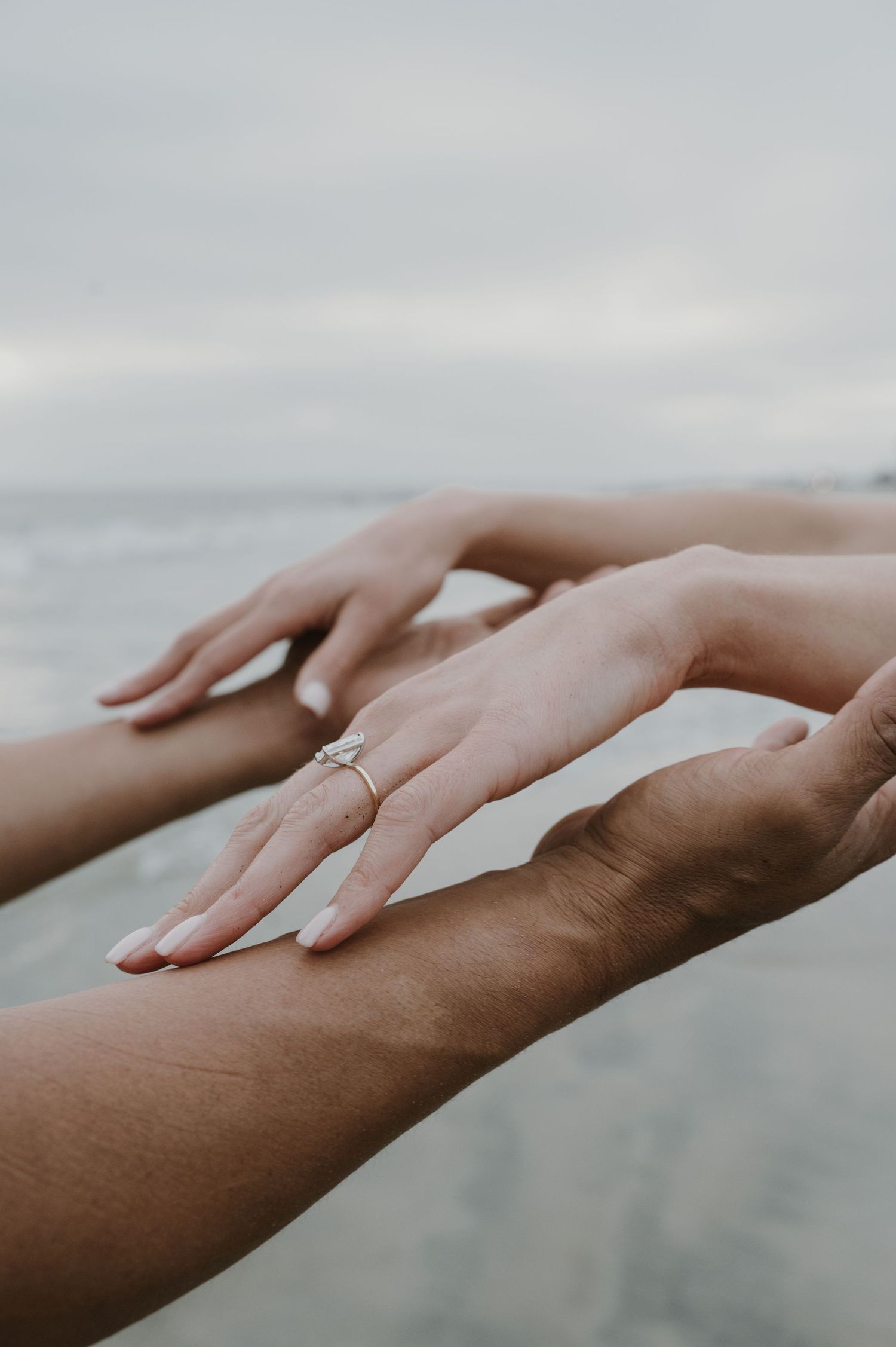 Close-up of hands with engagement ring against blurred ocean background.