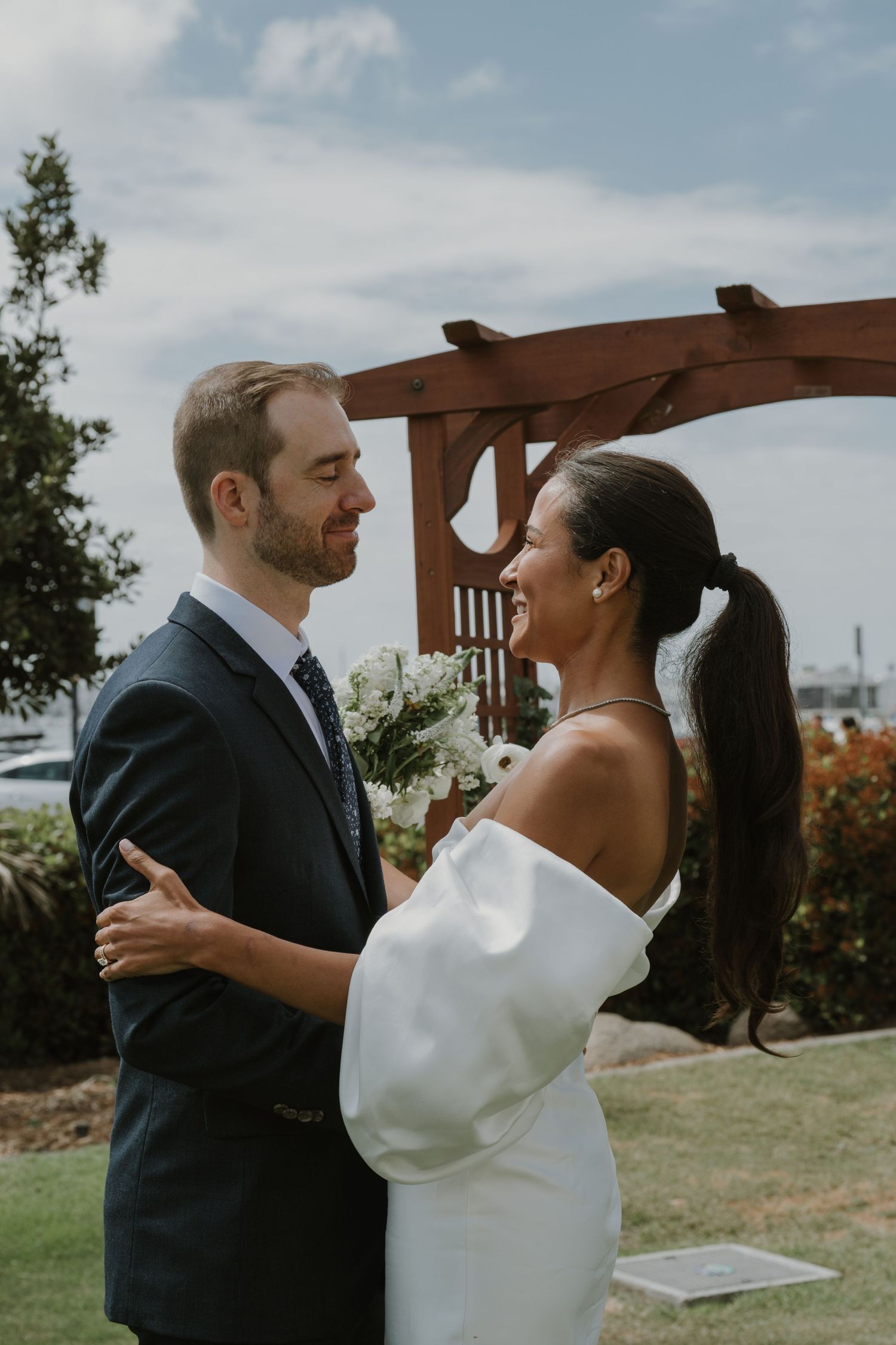 Wedding couple sharing intimate moments under wooden pergola by the coast.