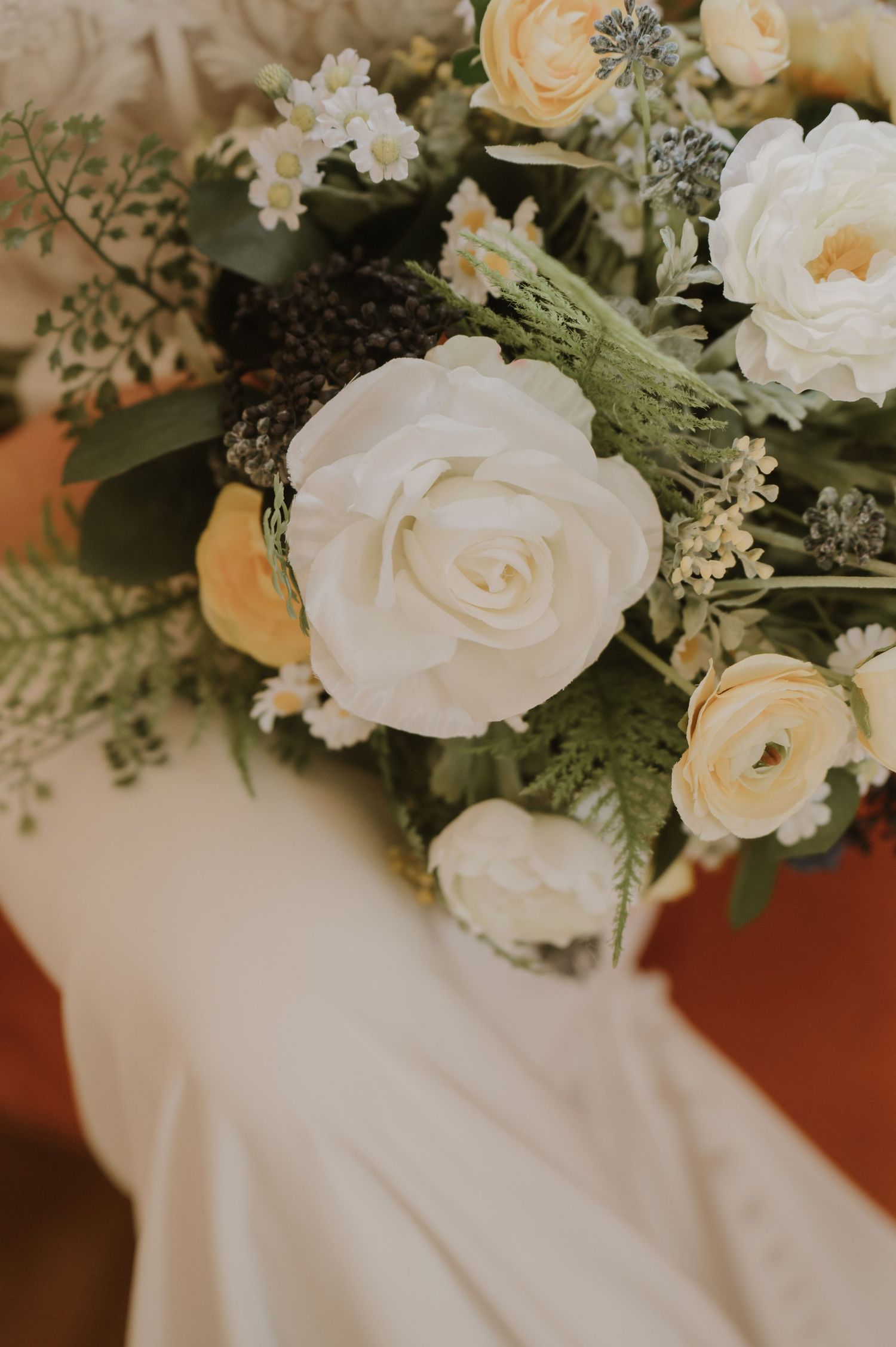 Delicate white and peach roses with greenery accent a wedding dress.